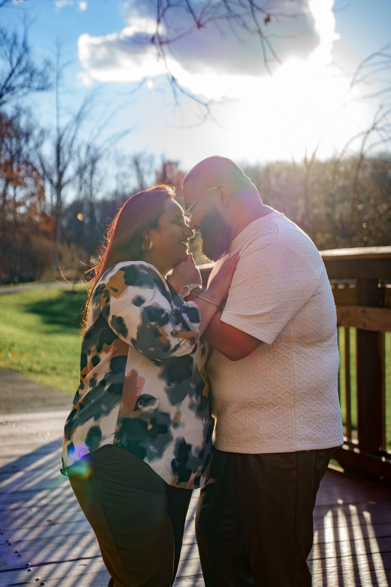 Couple embraces in silhouette against bright sunlight on wooden deck during romantic outdoor photo session.