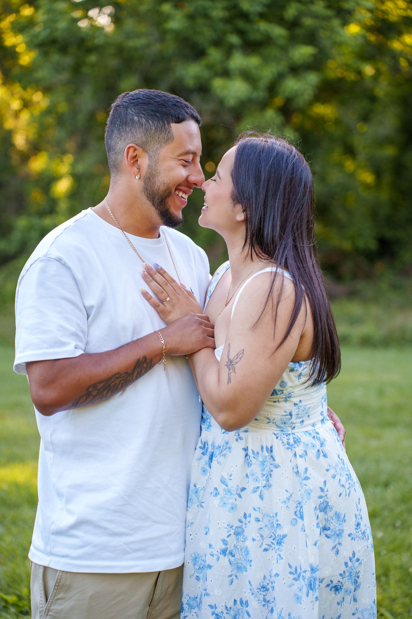 A smiling couple shares a romantic moment outdoors, the man in a white tee embracing a woman in a floral sundress.