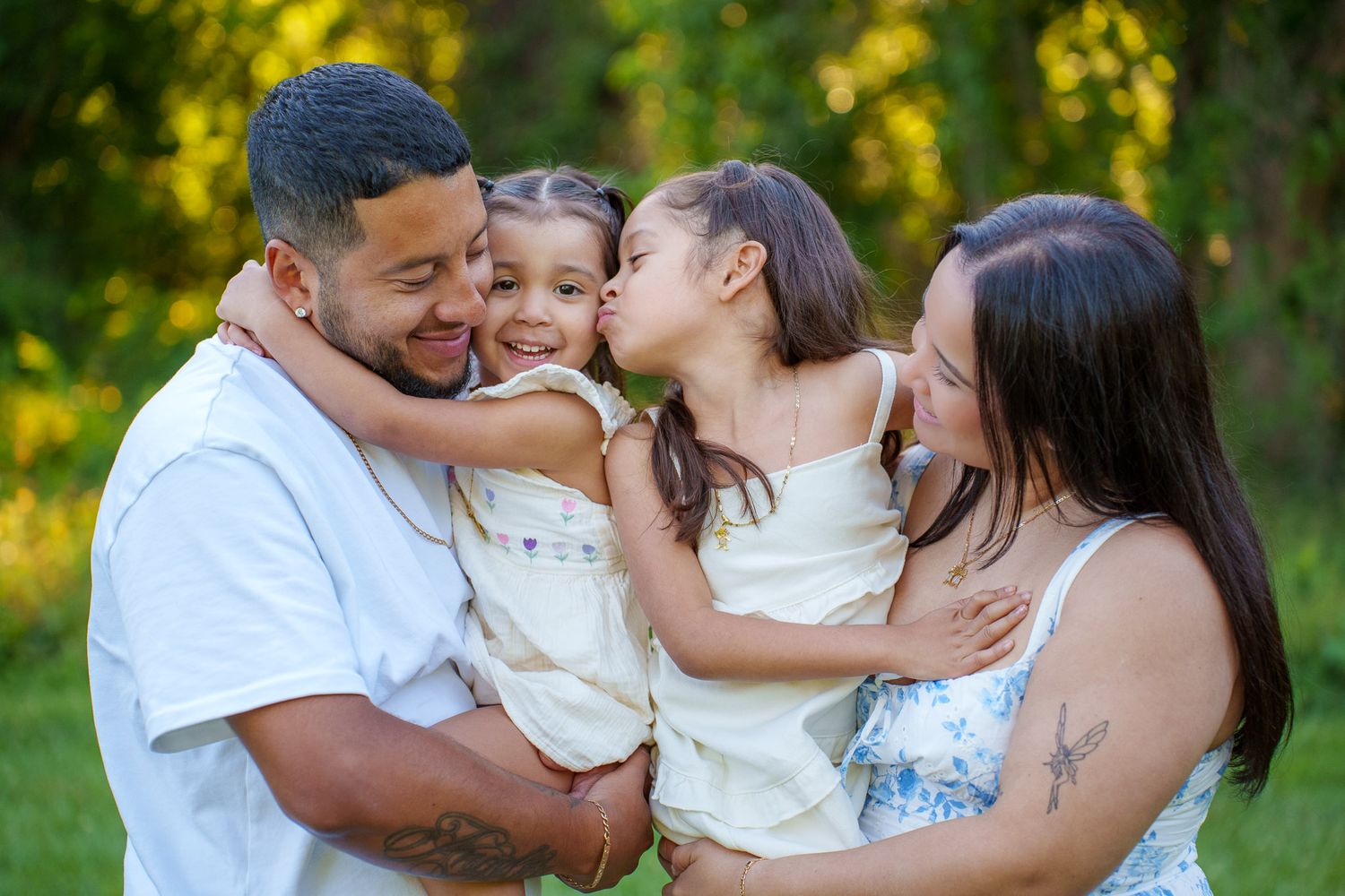 Happy family of four sharing a joyful moment outdoors, with two young girls hugging their smiling parents.