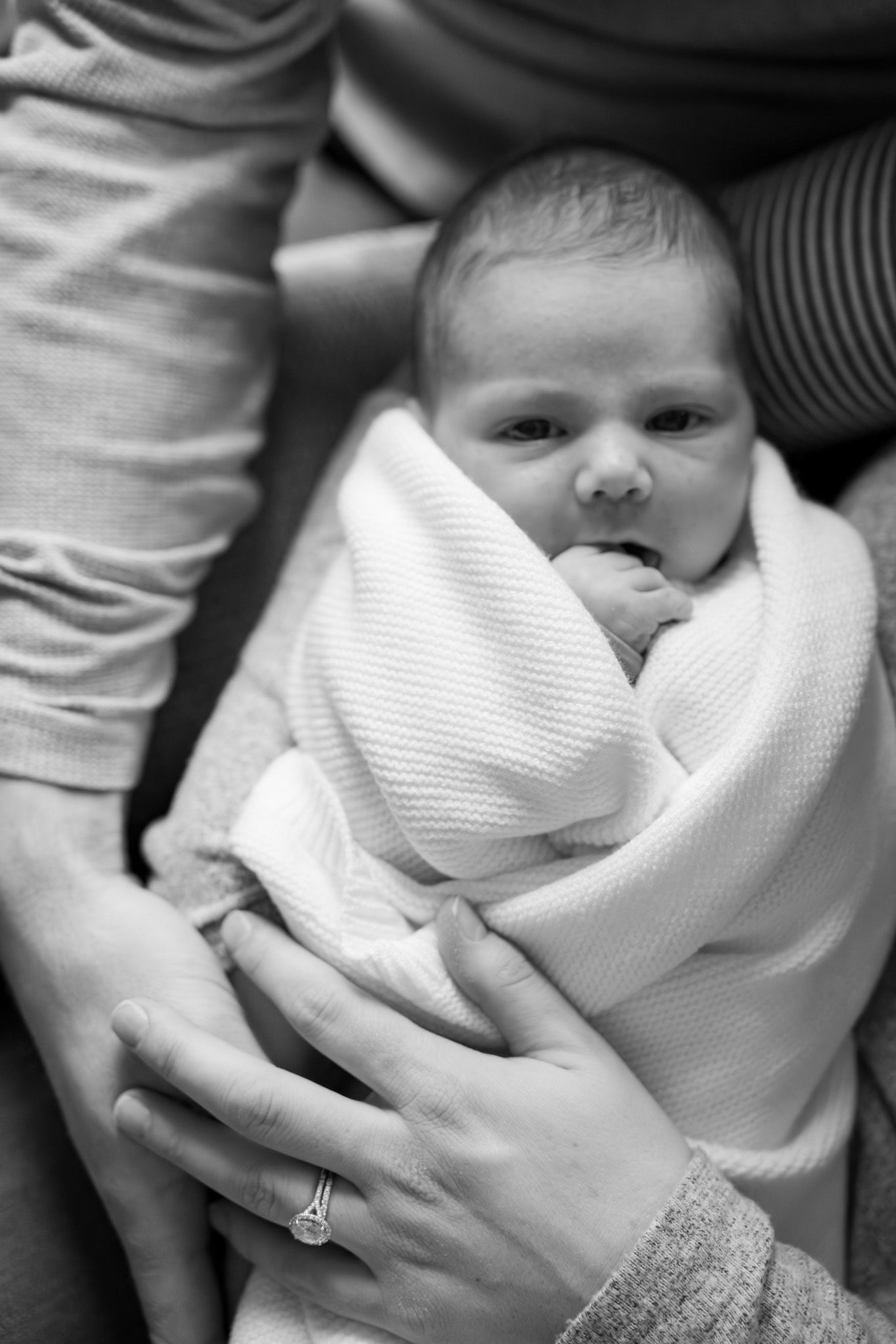A black and white photo series showing a baby wrapped in a white blanket being cradled in someone's arms.