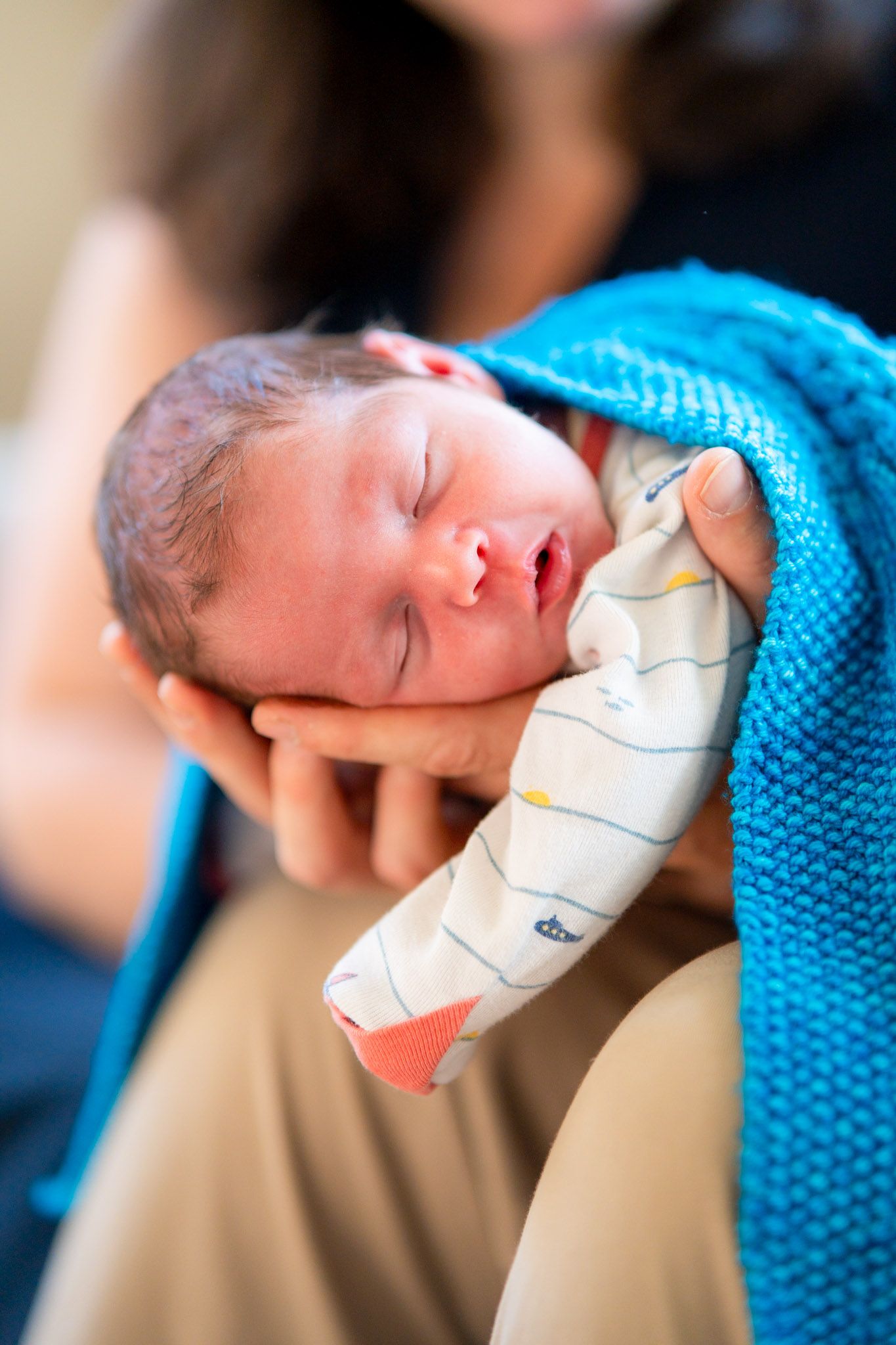 A newborn baby wrapped in a blue blanket sleeps peacefully while being cradled in someone's hands.