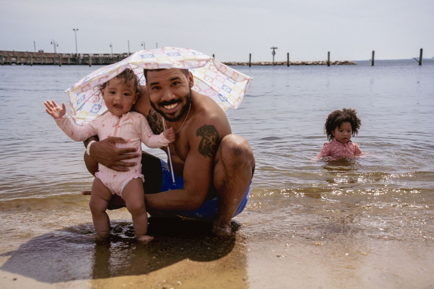 Family playing and splashing in shallow beach water on sunny day.