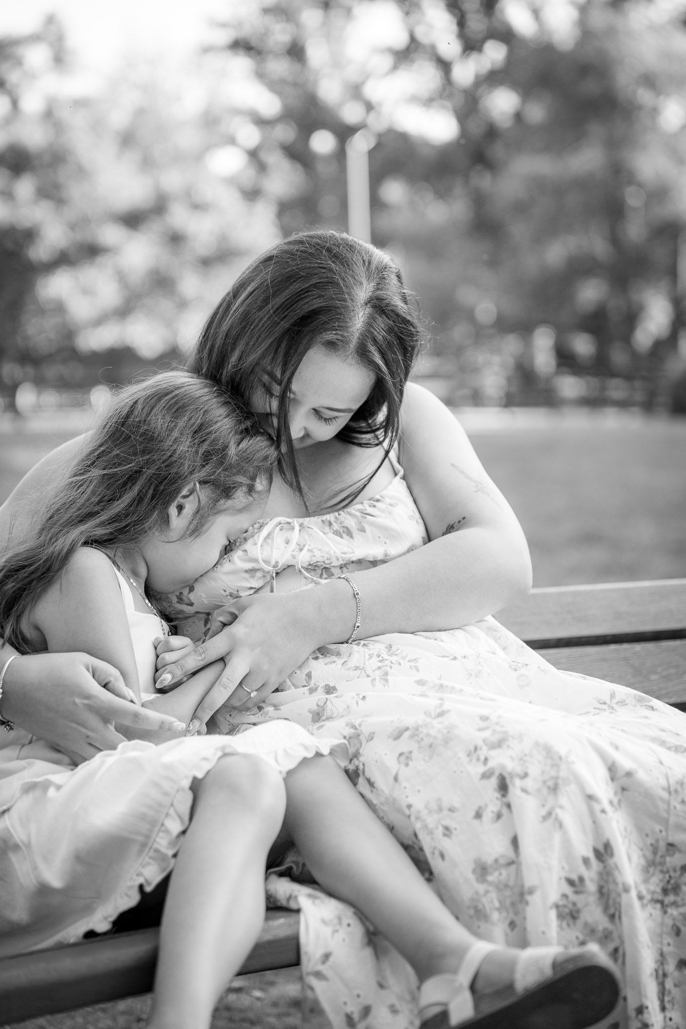 Black and white photo of a mother tenderly embracing two young daughters on a bench in a park.