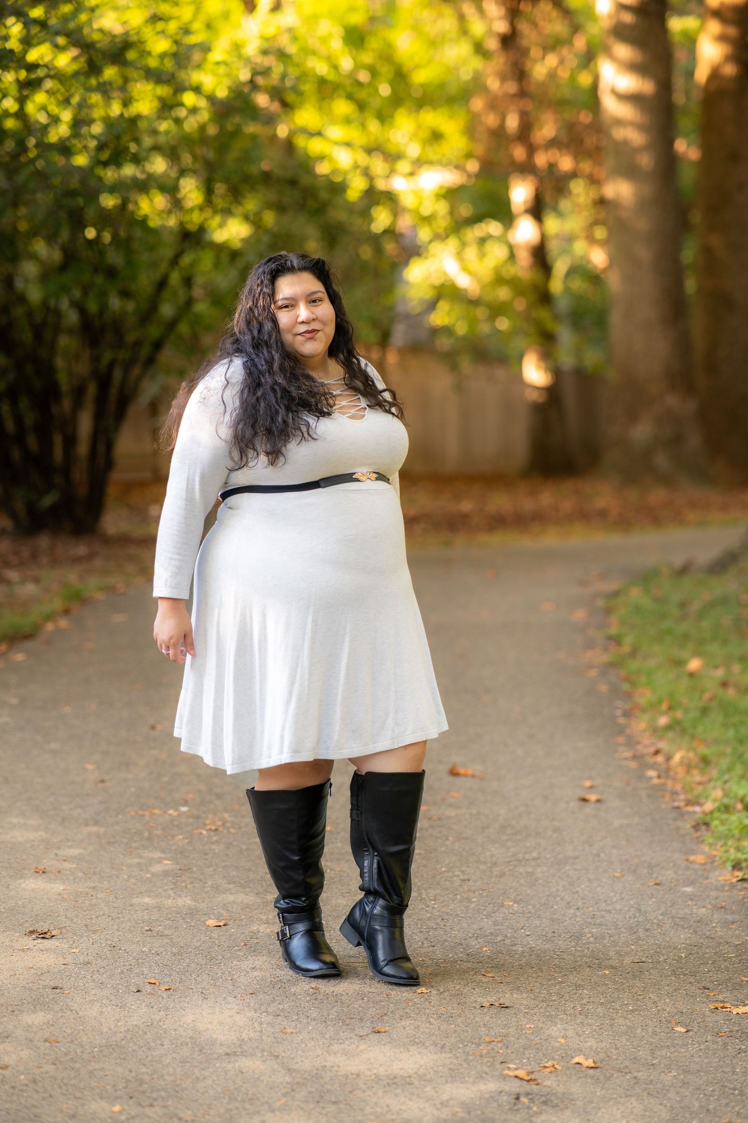 A solo portrait wearing a white flowing dress and black pants stands on an autumn path surrounded by golden foliage. Sligo Creek Trail