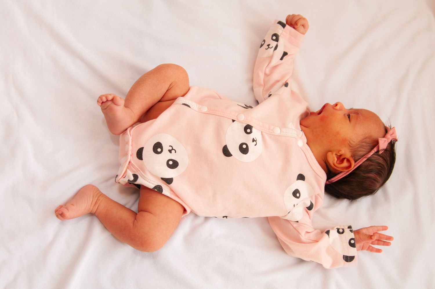Baby wearing panda-print onesie lying on white bedding for lifestyle newborn session in home in the DMV. Newborn details