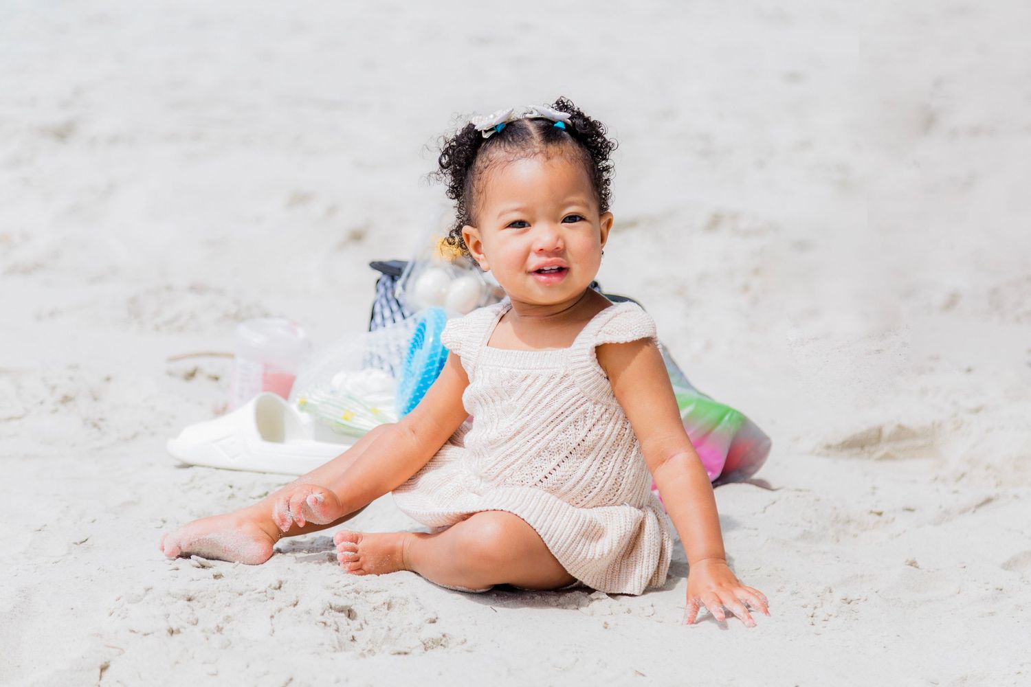 Baby in white dress crawling on sandy beach.
