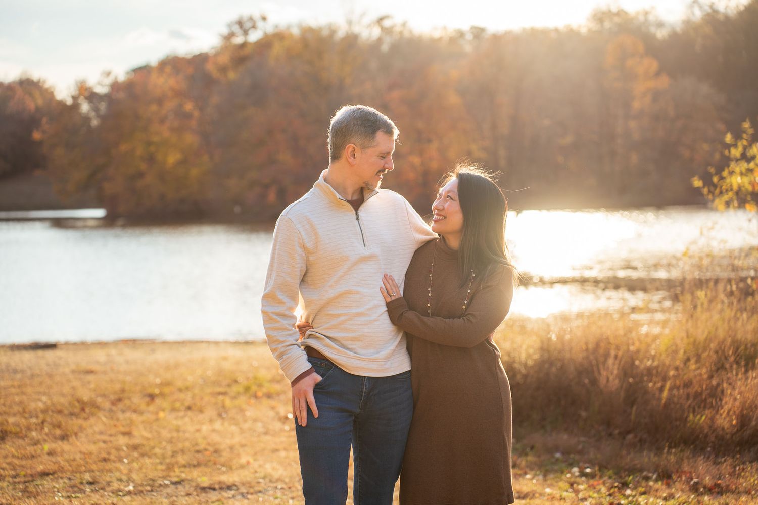 A couple shares a tender moment in a sunlit field during golden hour at sunset.