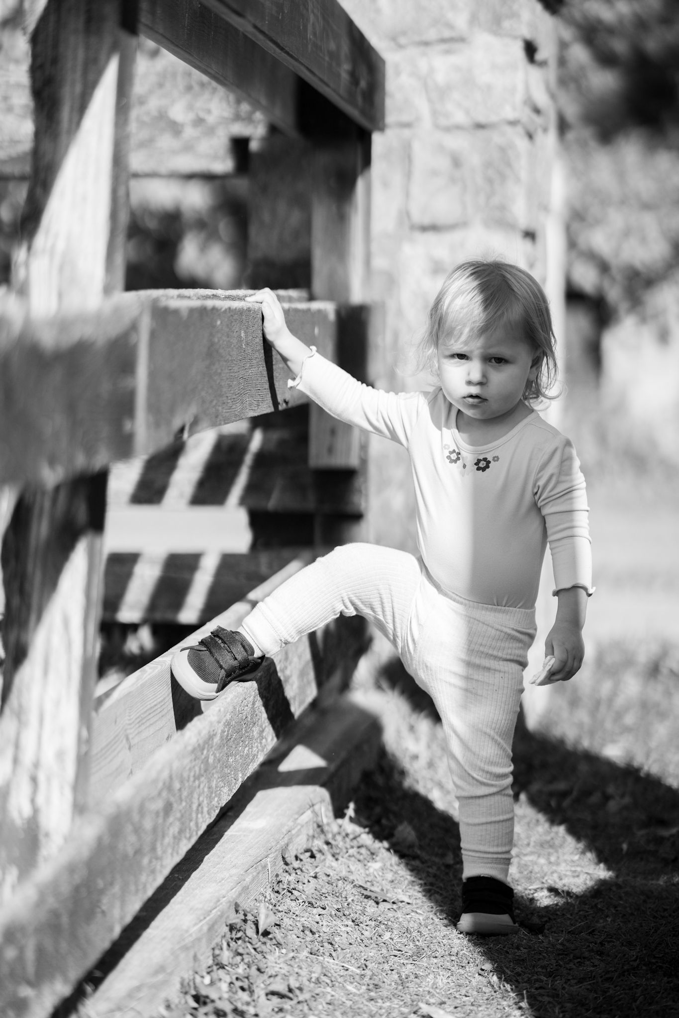 A child in a white shirt plays in dirt and soil near wooden posts in a black and white photograph.