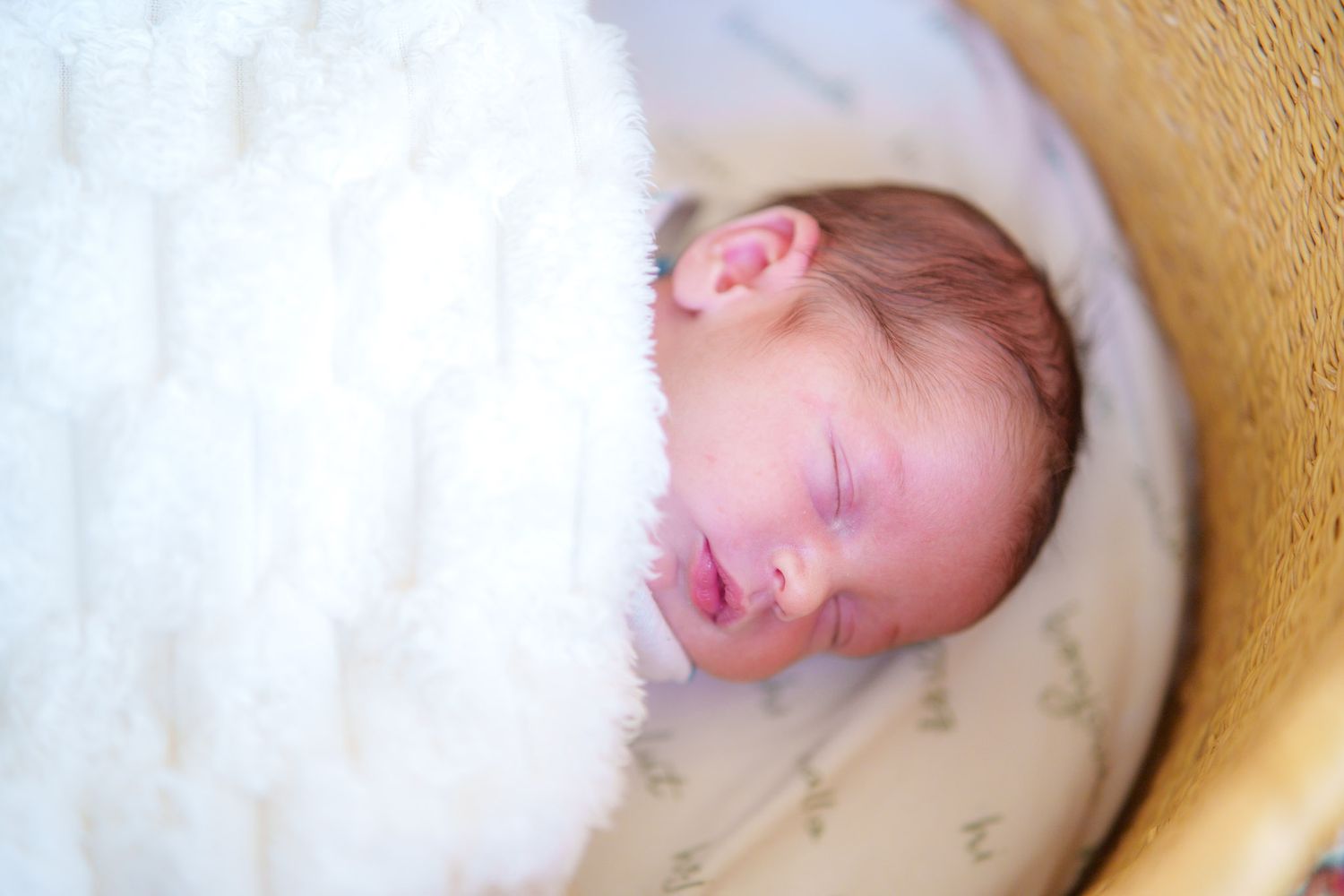 A sleeping baby lies peacefully in a white blanket against a soft beige background.