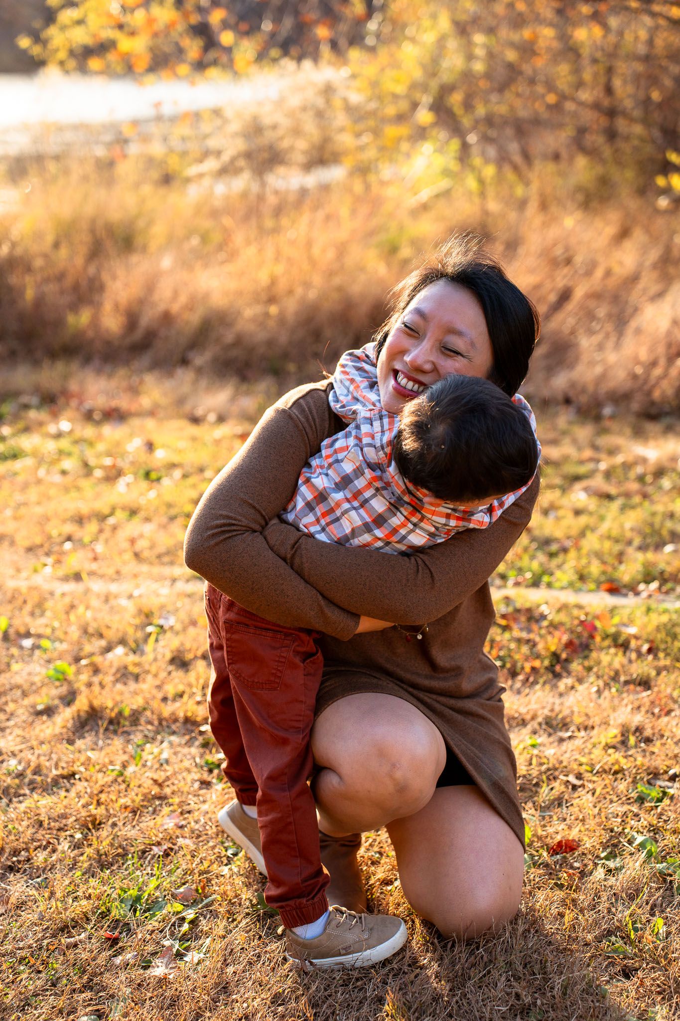 A child in a brown coat and plaid shirt plays outdoors in golden autumn sunlight.