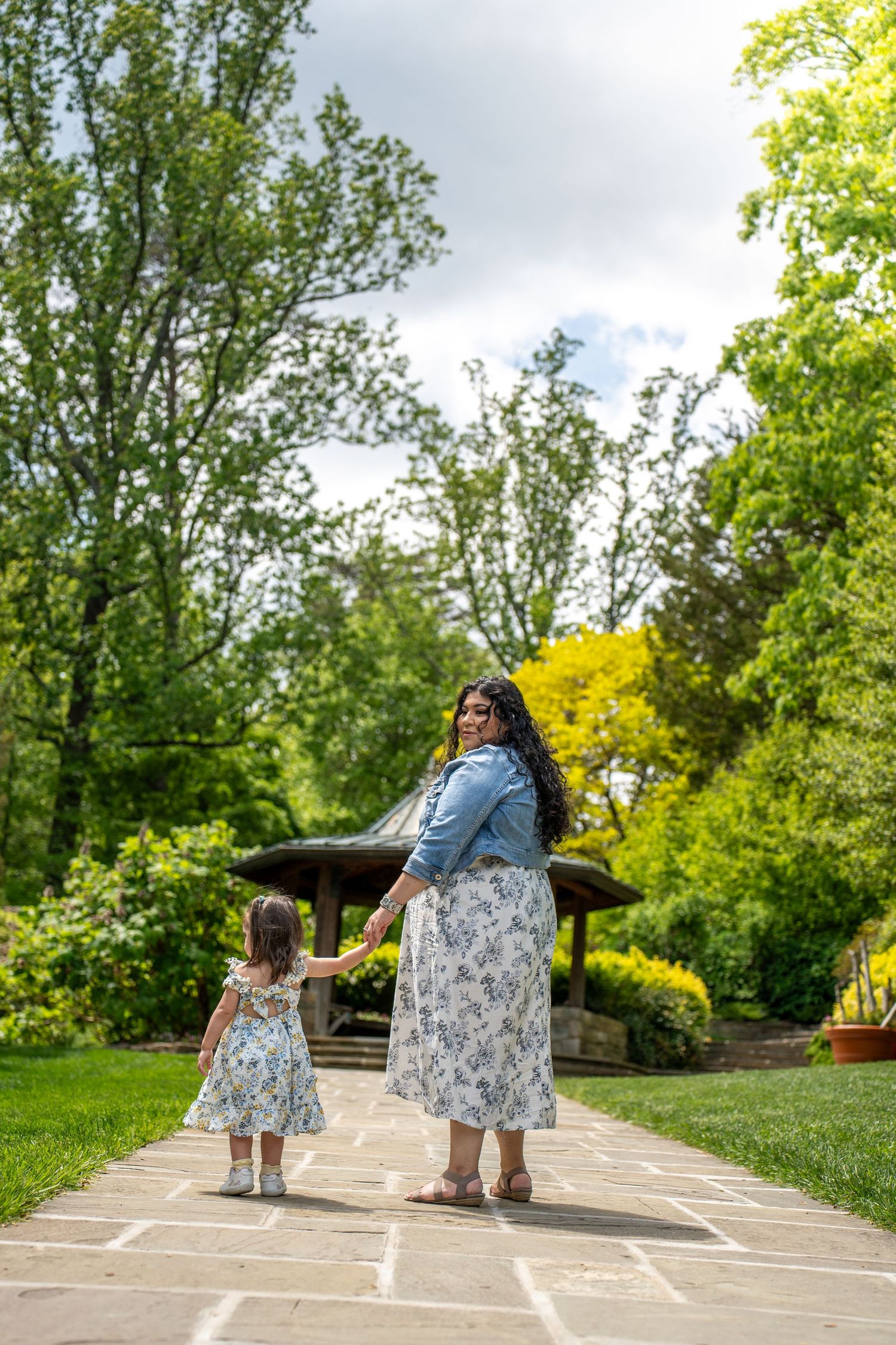 Mom and daughter standing together on a stone path in a lush garden setting on a bright spring day. Brookside Garden
