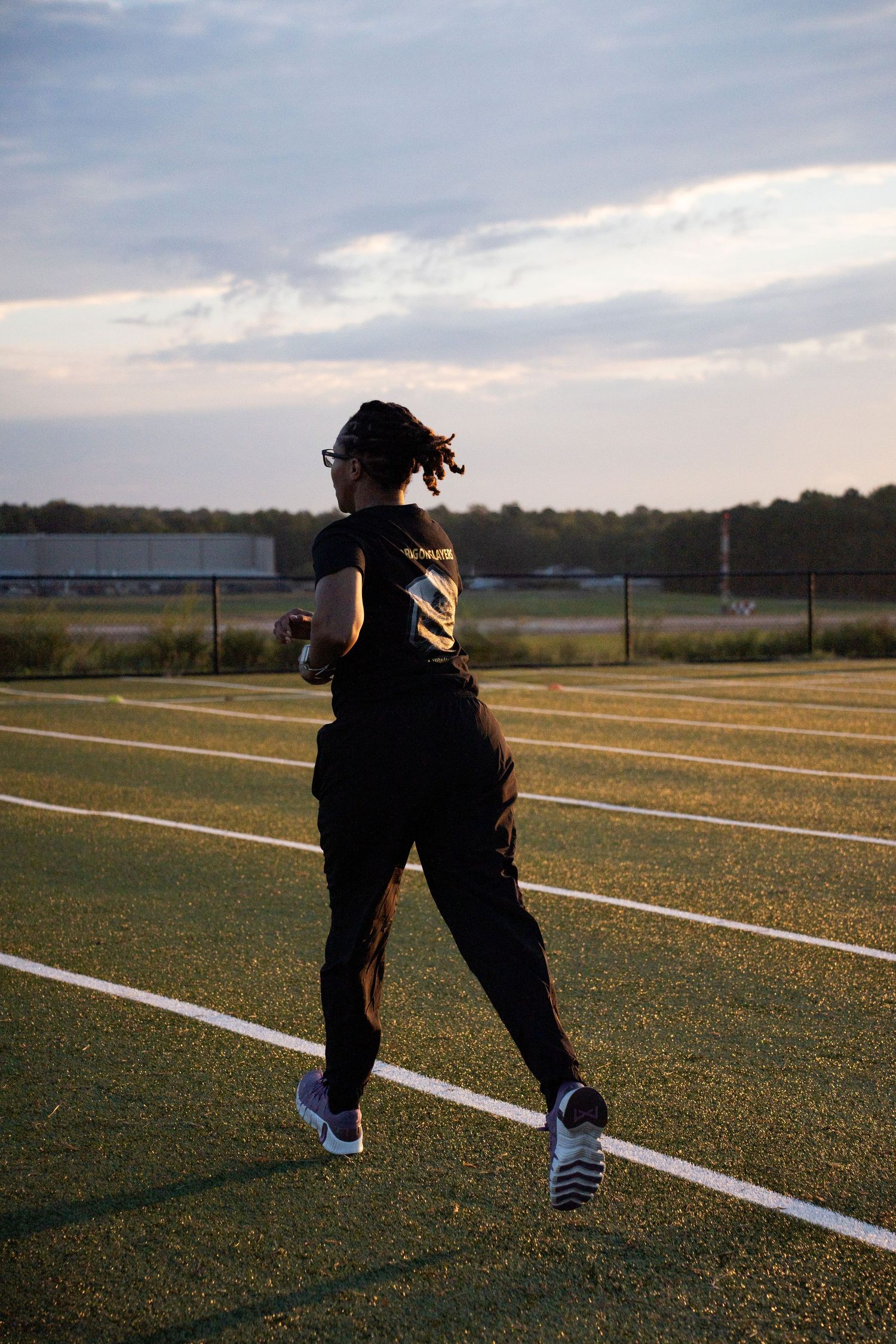 Runner silhouetted against cloudy sky exercising alone on athletic track during sunset.