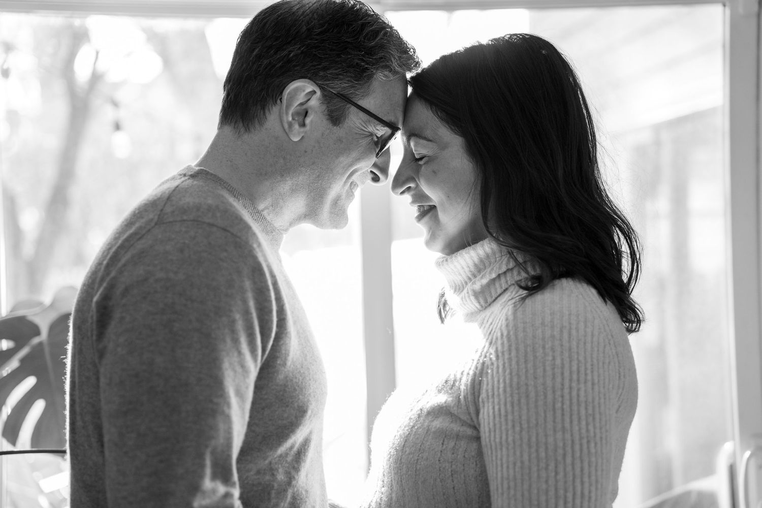A series of black and white romantic photos showing tender moments between a couple by a window.