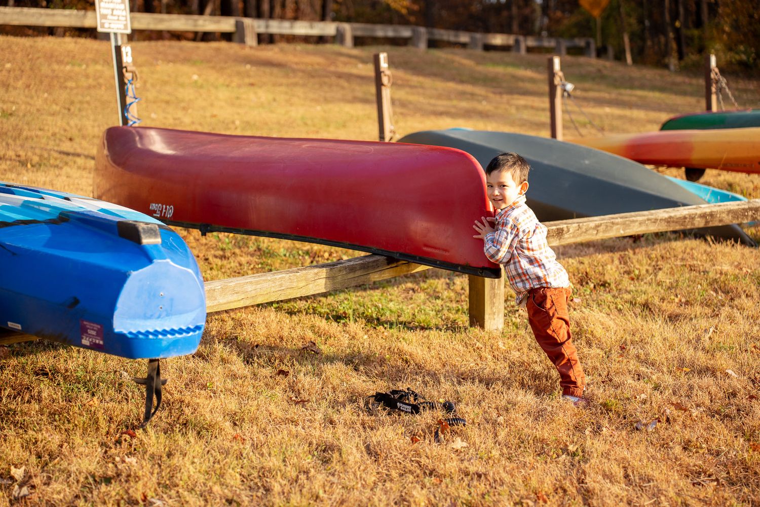 A child plays near colorful kayaks on the shore during a fall afternoon.