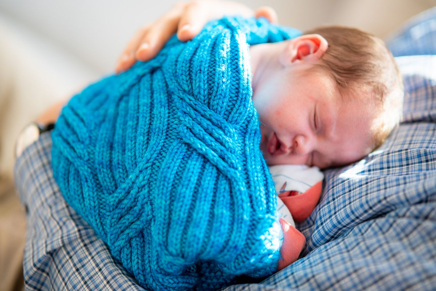 A person wearing a blue knit hat rests their head on a plaid pillow while sleeping.