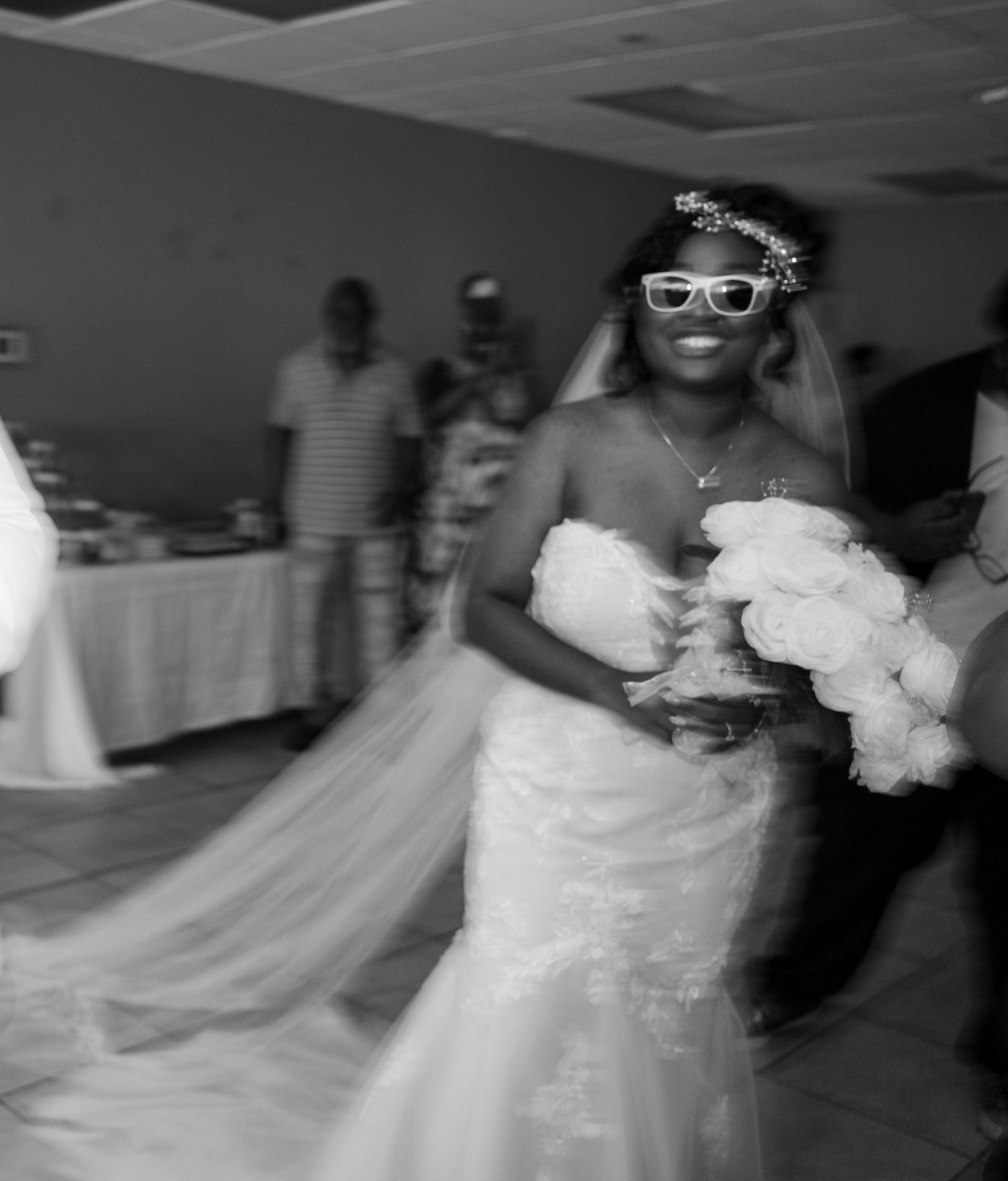A wedding party dances and celebrates in a reception hall with flowing white dresses and formal attire.