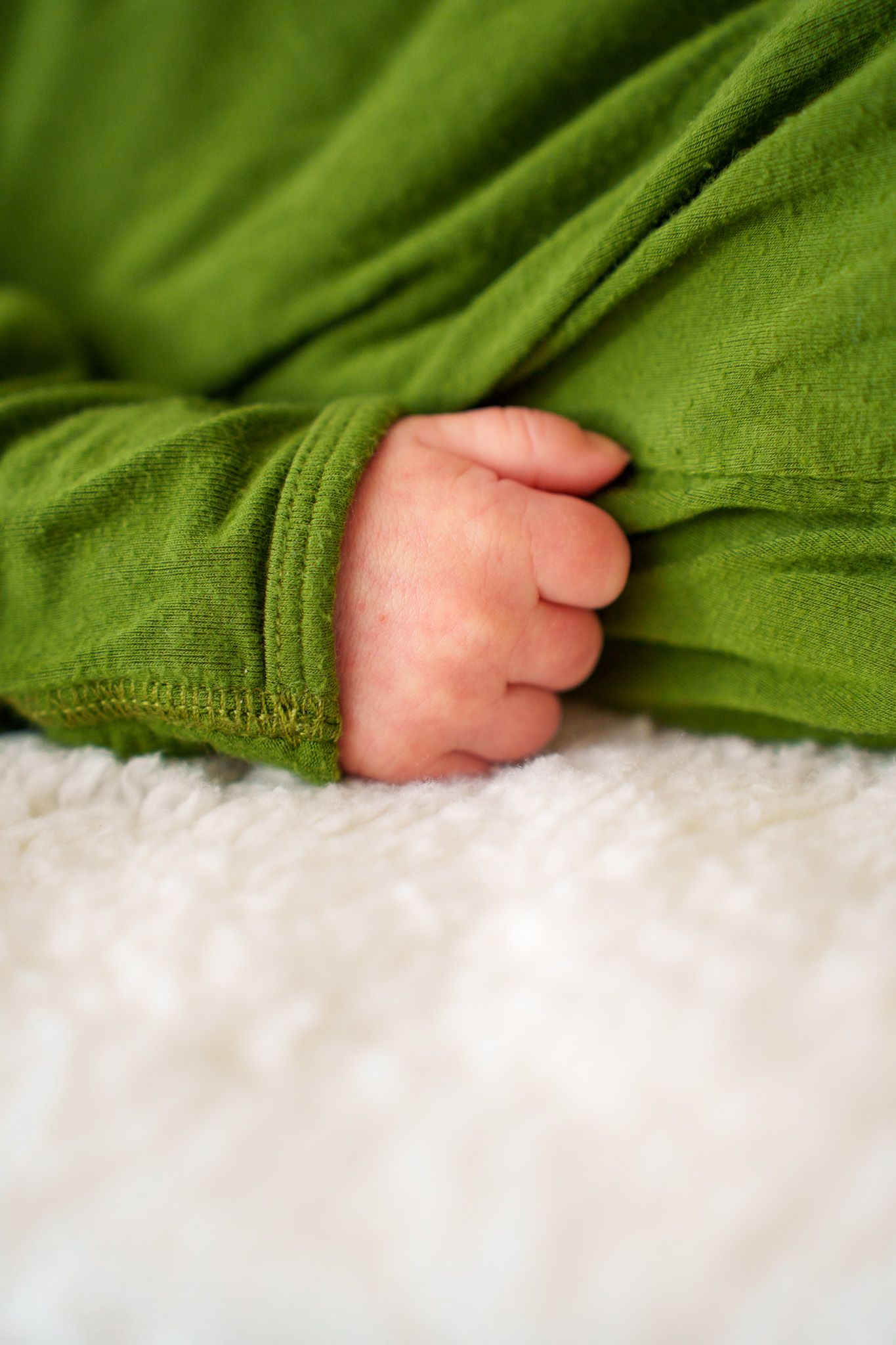 A tiny baby's foot peeks out from under a soft green blanket against white bedding.