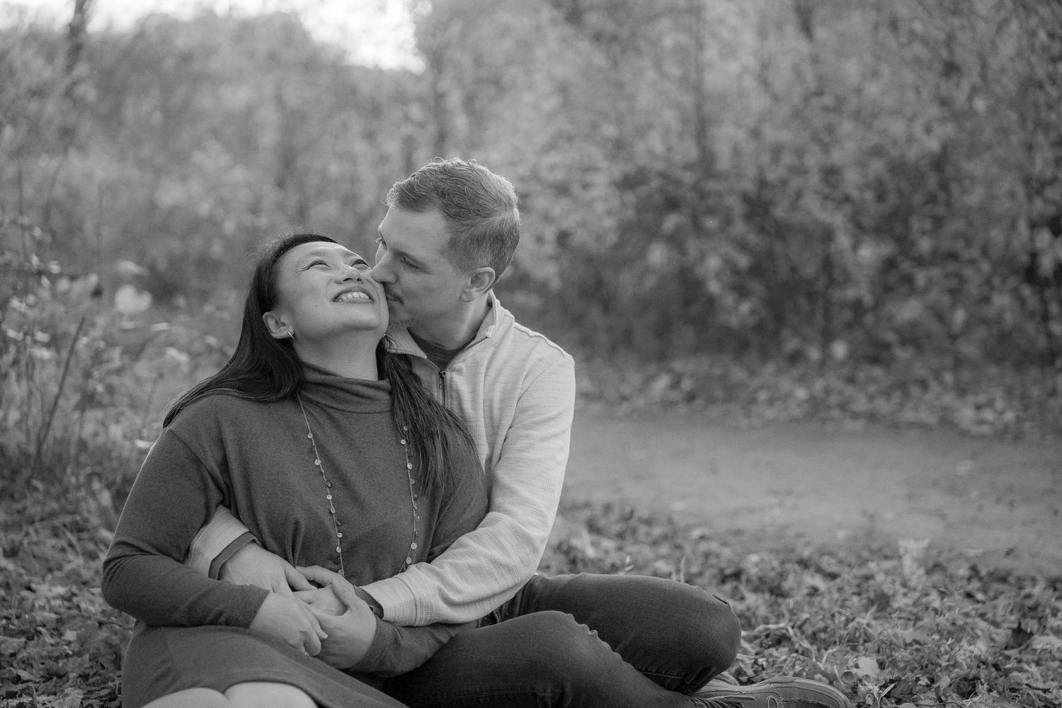 A series of black and white romantic photos showing a couple embracing and kissing outdoors in a natural setting.