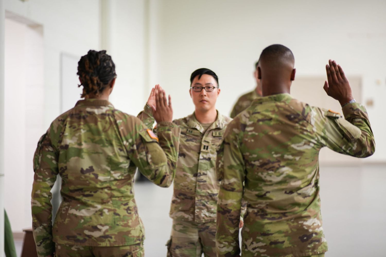 Military service members in camouflage uniforms stand in formation with raised hands during a ceremony.