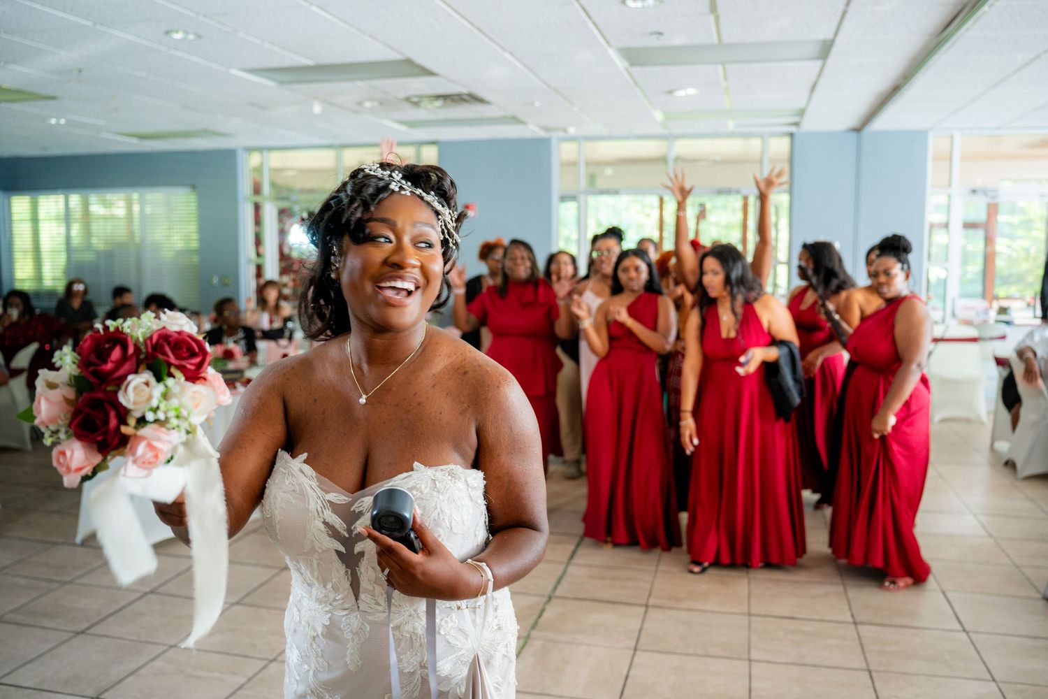 A wedding party wearing red dresses poses together in a bright indoor venue for formal photos.