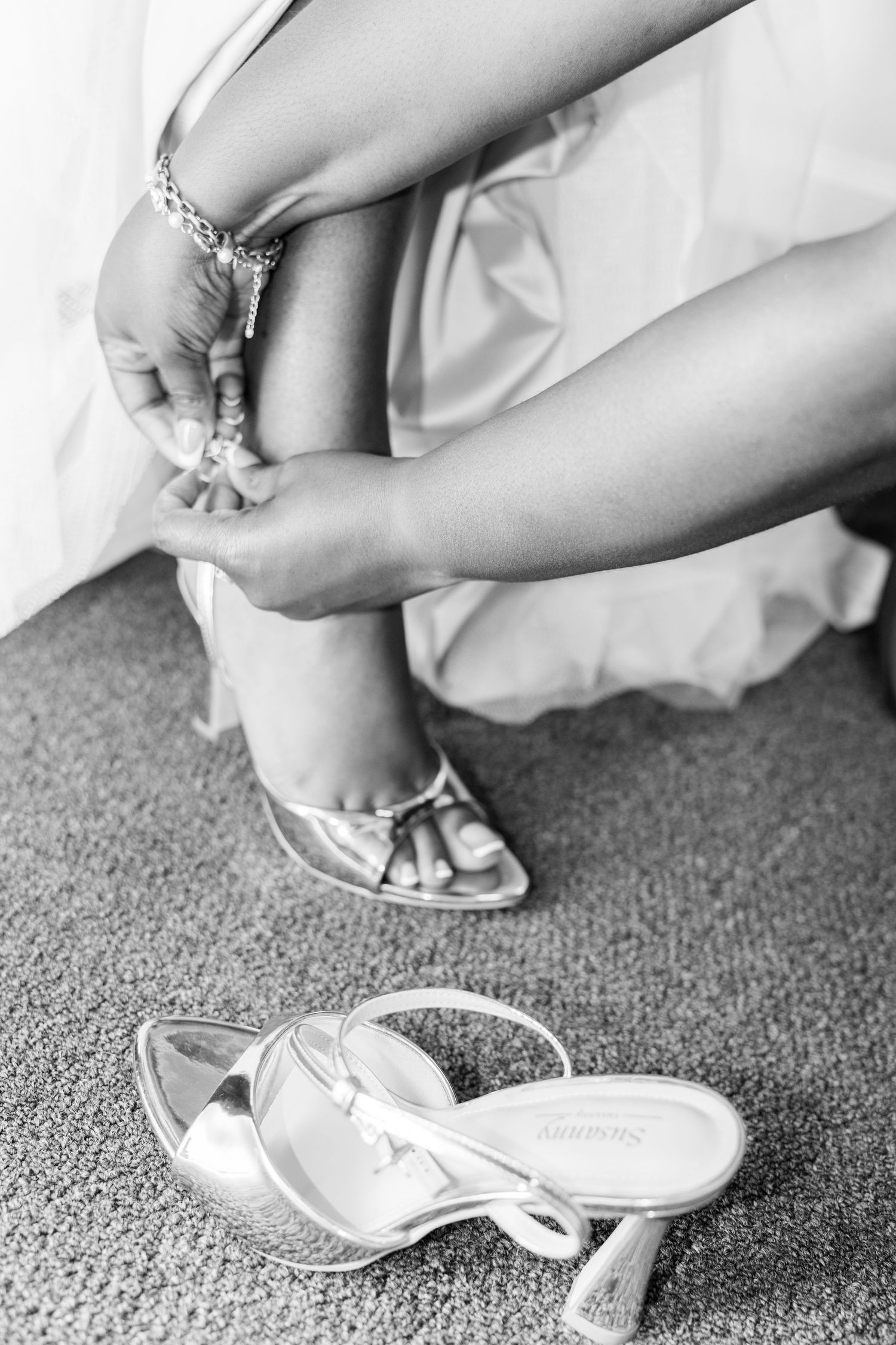 A series of black and white photos showing elegant bridal shoes being put on with white dress fabric flowing around them.