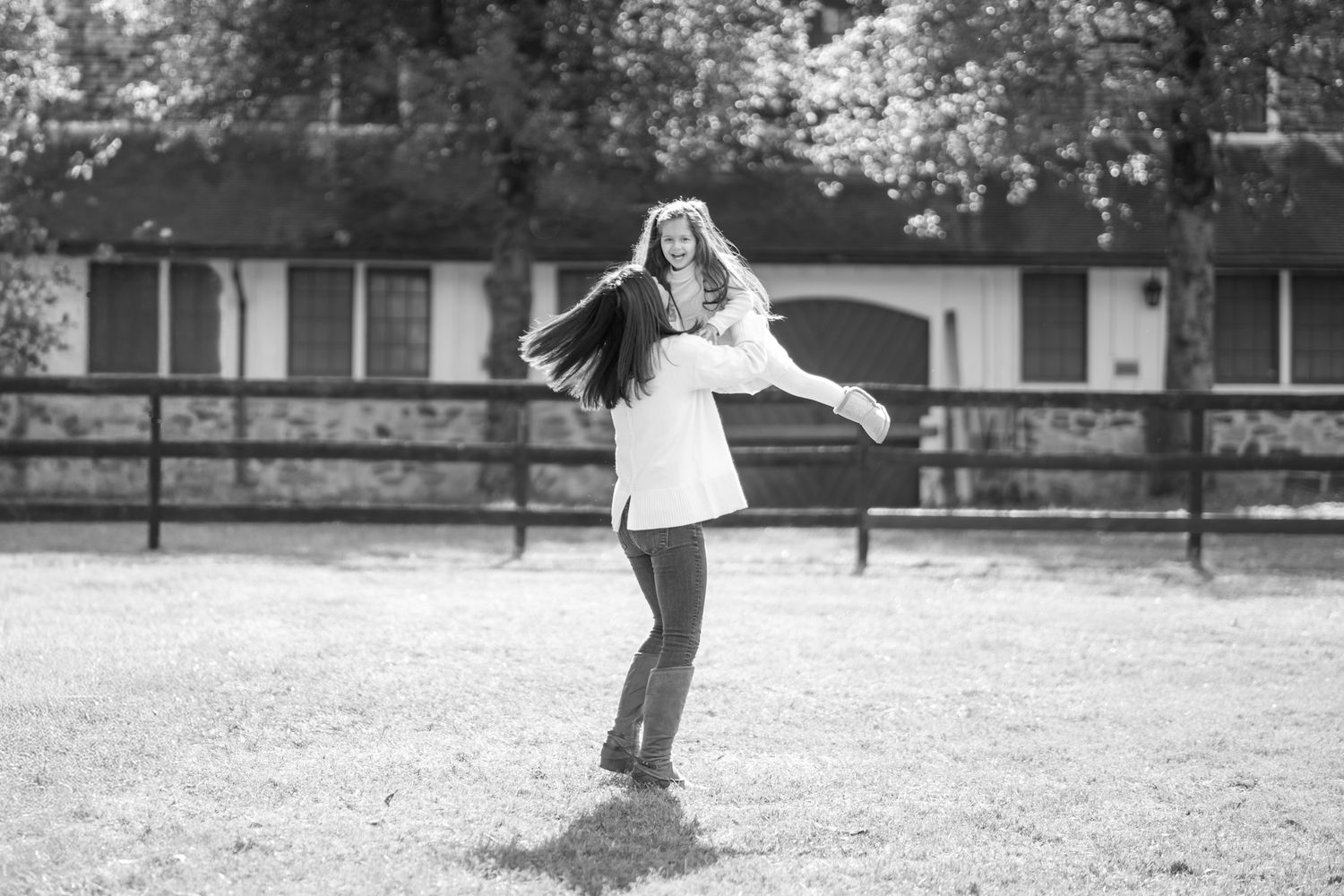 A person in a white dress spins joyfully in a field with a wooden fence and building in the background.