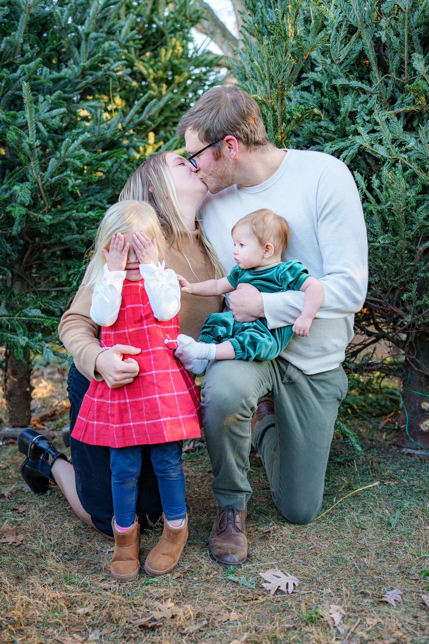An intimate family portrait among evergreen trees at a Christmas tree farm.