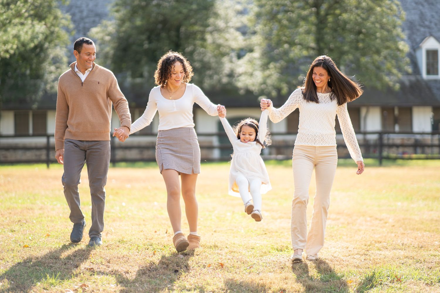 Family holding hands and running together through a sunny field on a warm autumn day.