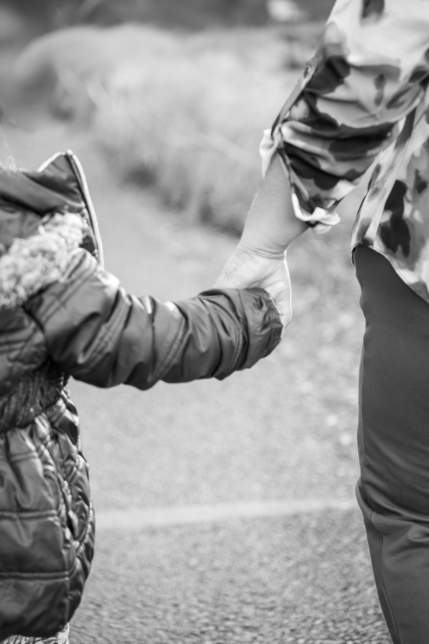 A black and white photo shows a person's hand holding a smartphone while walking outdoors.