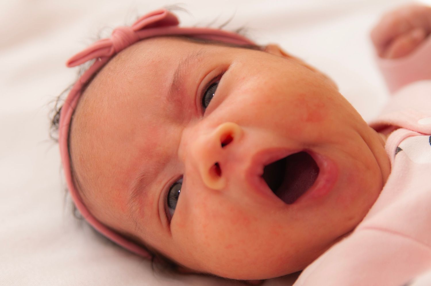 Newborn baby yawning while lying on white bedding for a lifestyle newborn session. Newborn Details. SIlver Spring, Maryland
