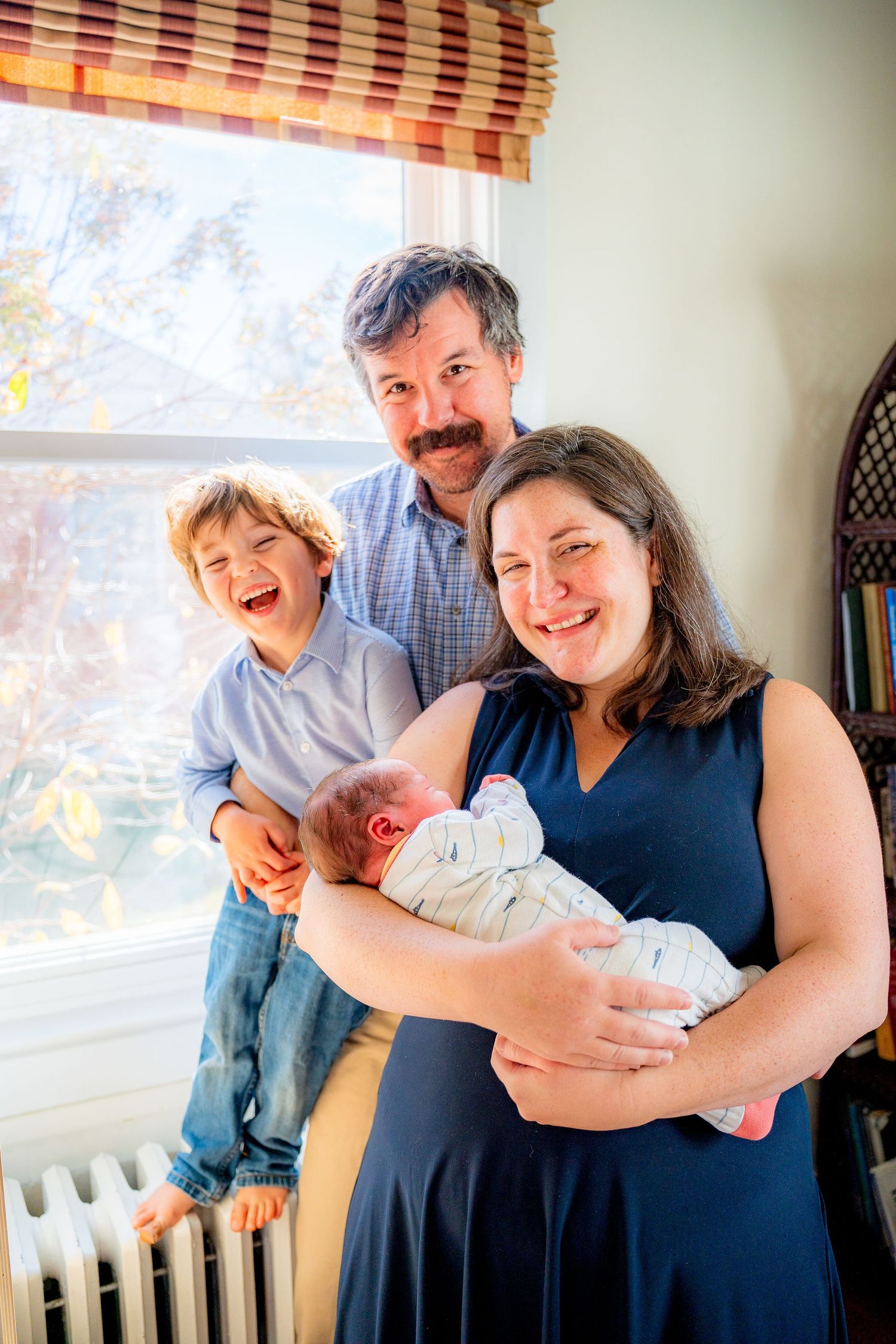 A joyful family moment showing a group gathered around a newborn baby in a sunlit room.