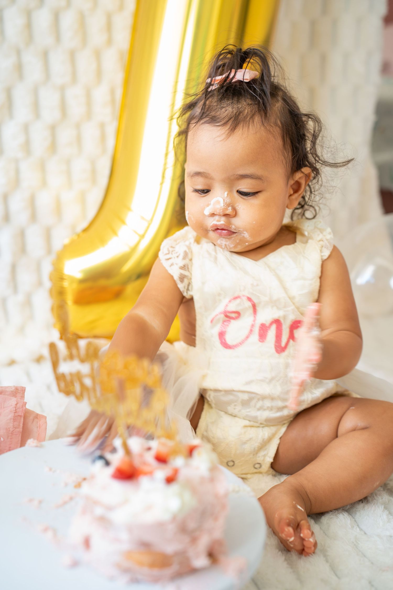 Sweet moments captured during baby's cake smash session with gold balloon and white backdrop.