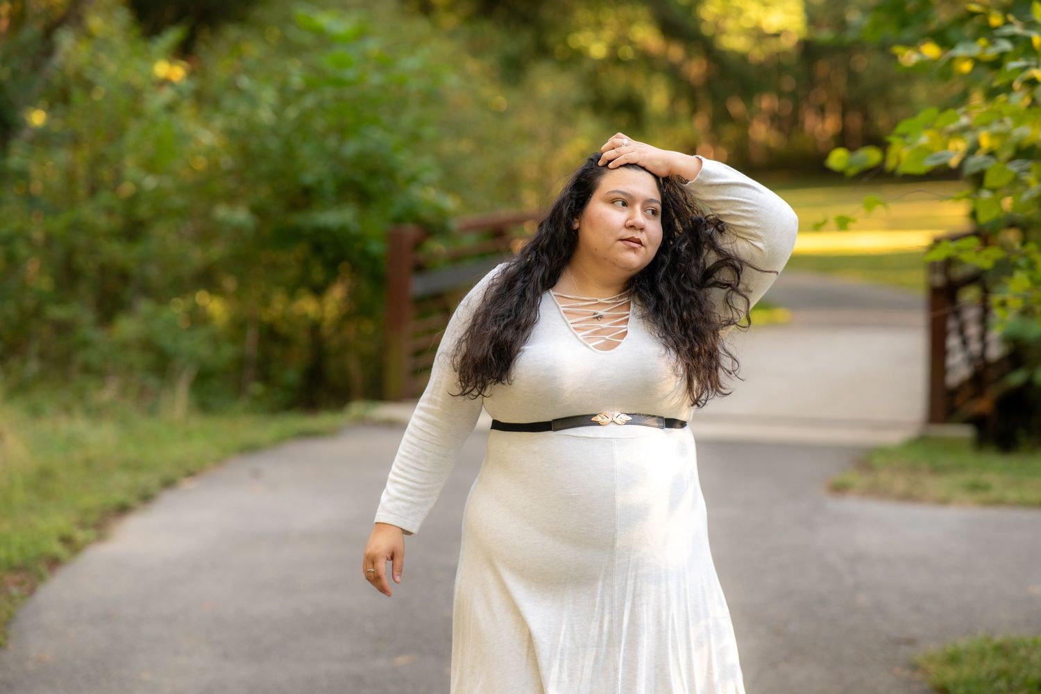 A person in a flowing white dress walks along a tree-lined path on an autumn day.