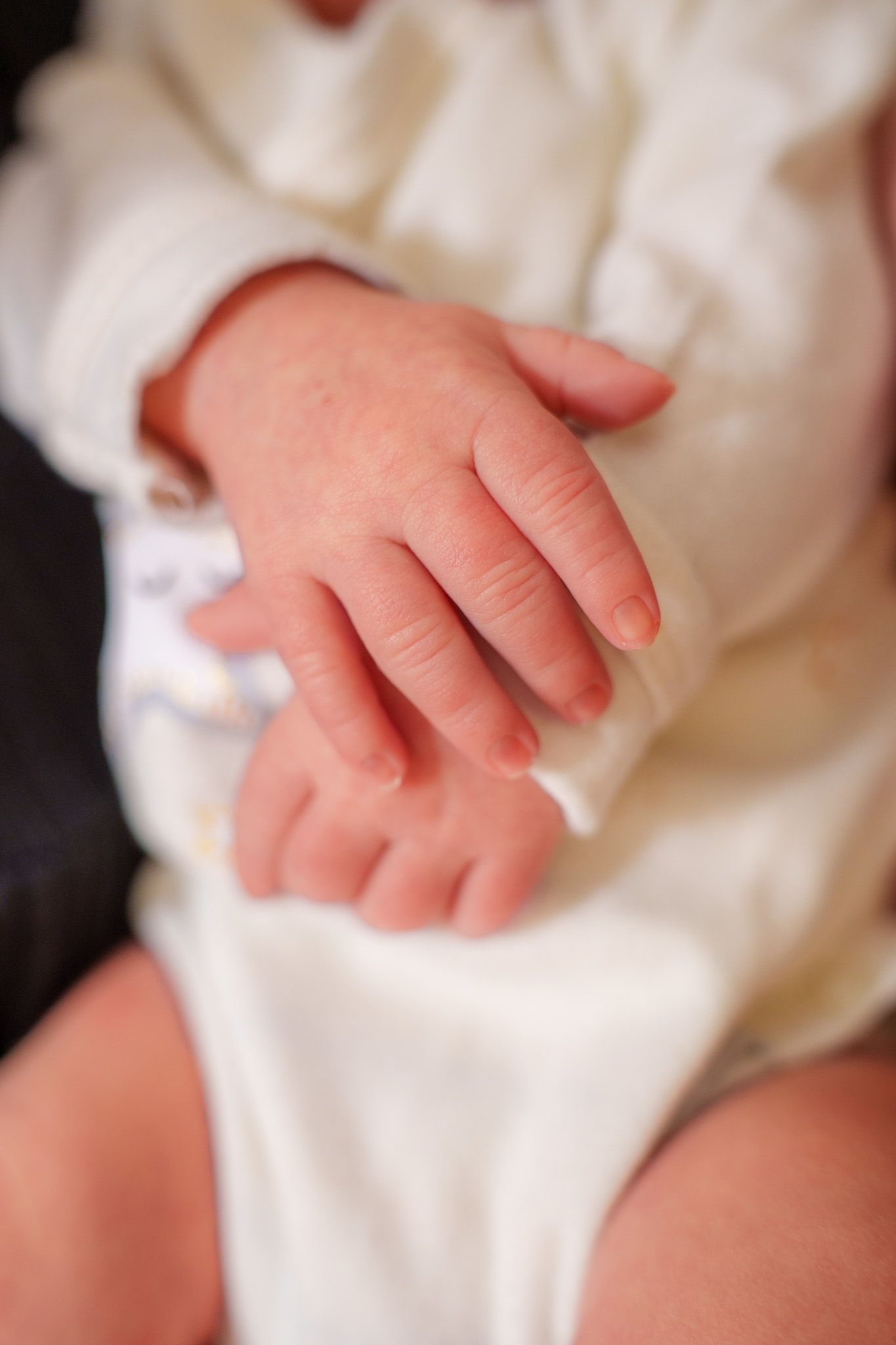 Close-up view of a baby's tiny hand grasping white fabric showing delicate fingers and soft skin texture.