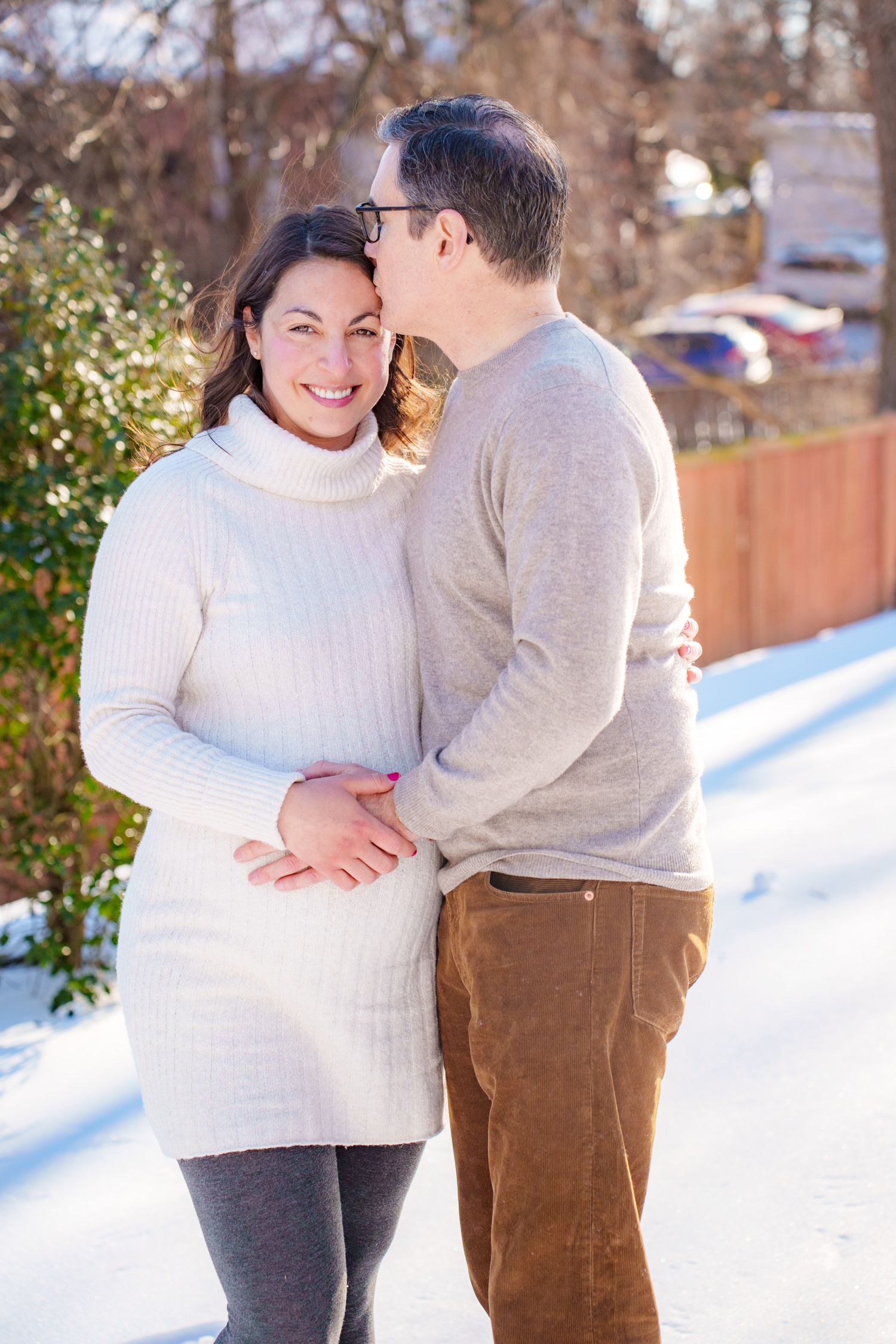 A couple shares a romantic moment in the snow, wearing winter clothing and embracing each other warmly.