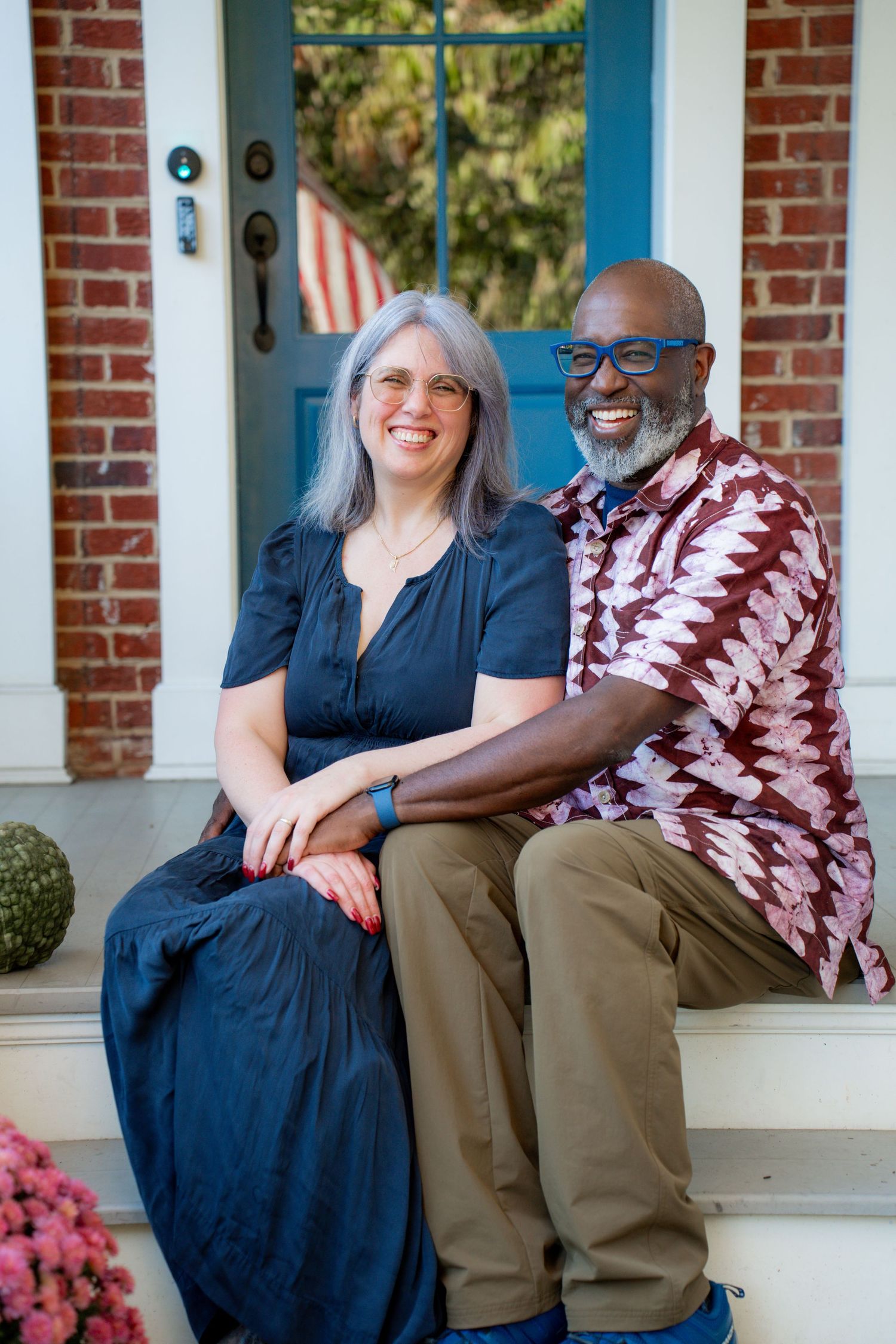 A couple sits together on a white porch with brick walls, sharing warm smiles and casual moments.