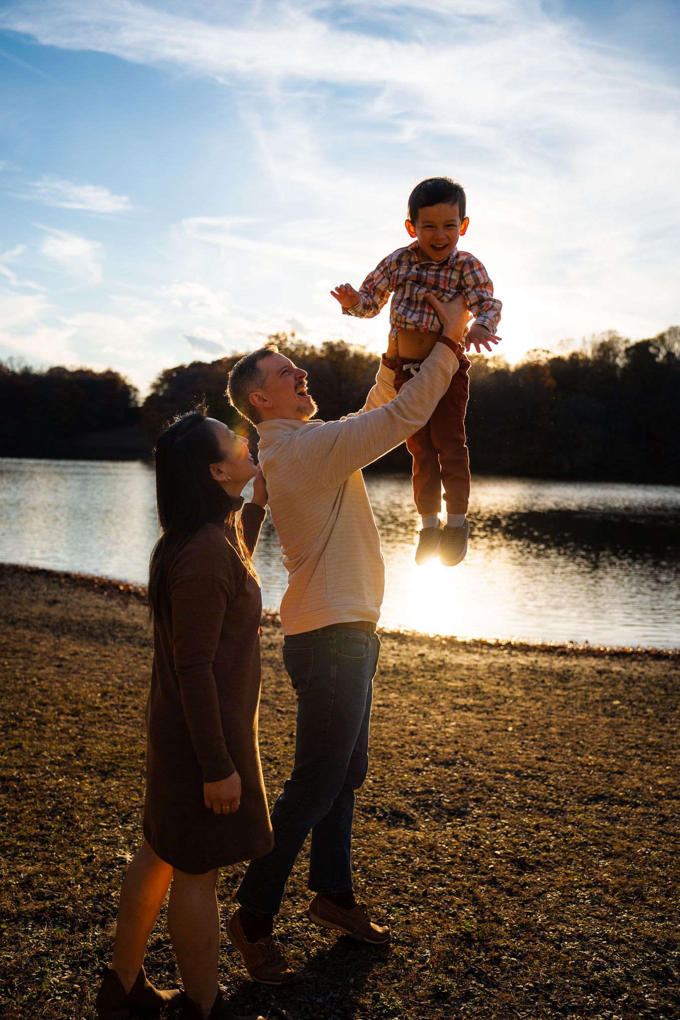 A family shares a playful moment at sunset by the lake with golden backlighting.