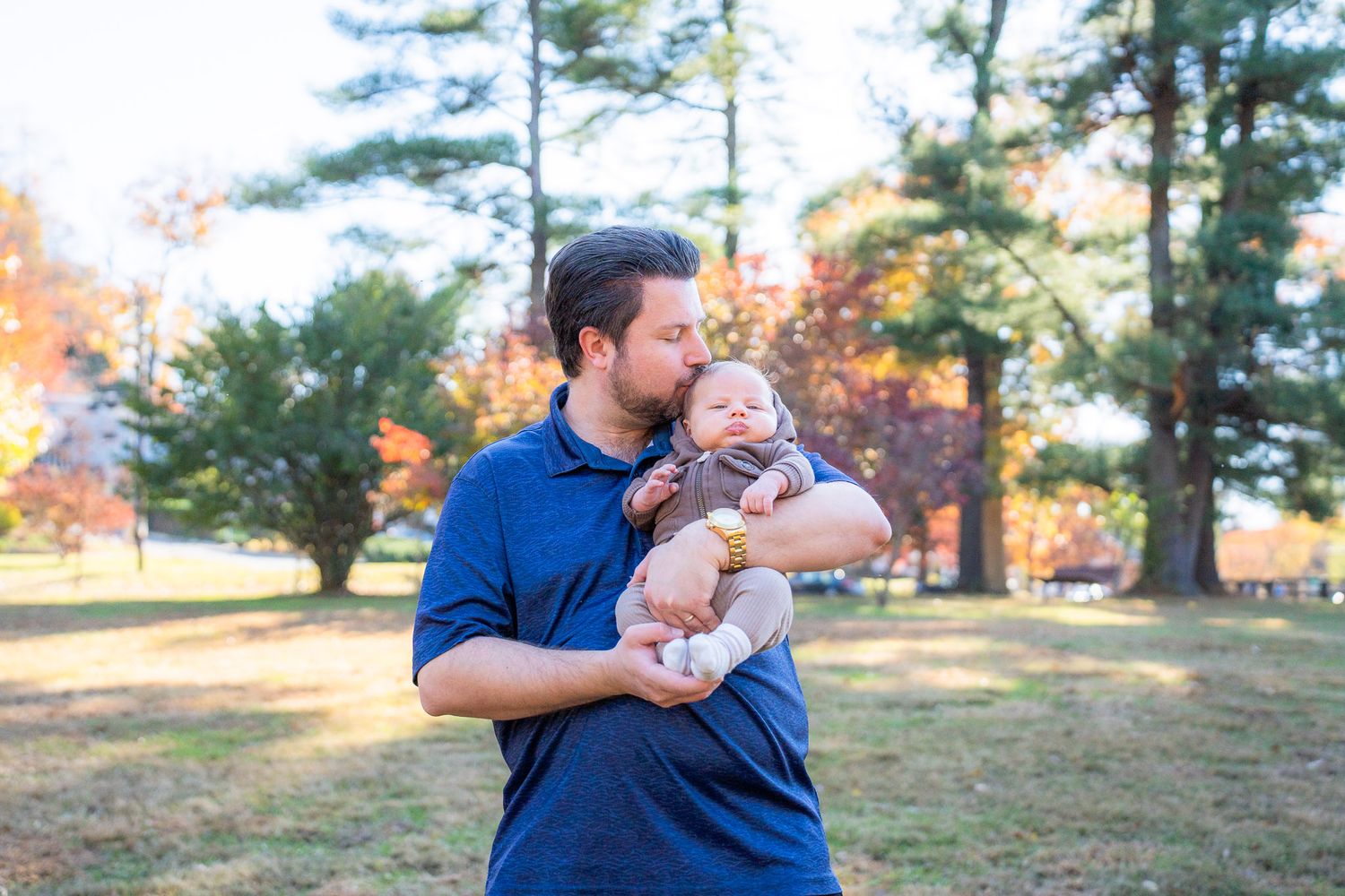 A family in coordinating blue outfits poses together outdoors during an autumn photoshoot session.