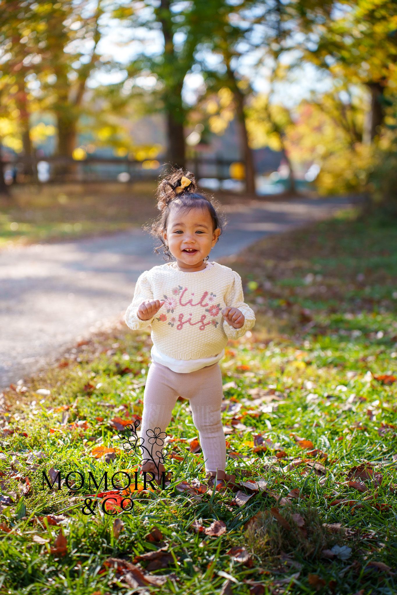 A toddler plays joyfully among colorful autumn leaves scattered on the ground during a sunny fall day at Clark Elioak Farm