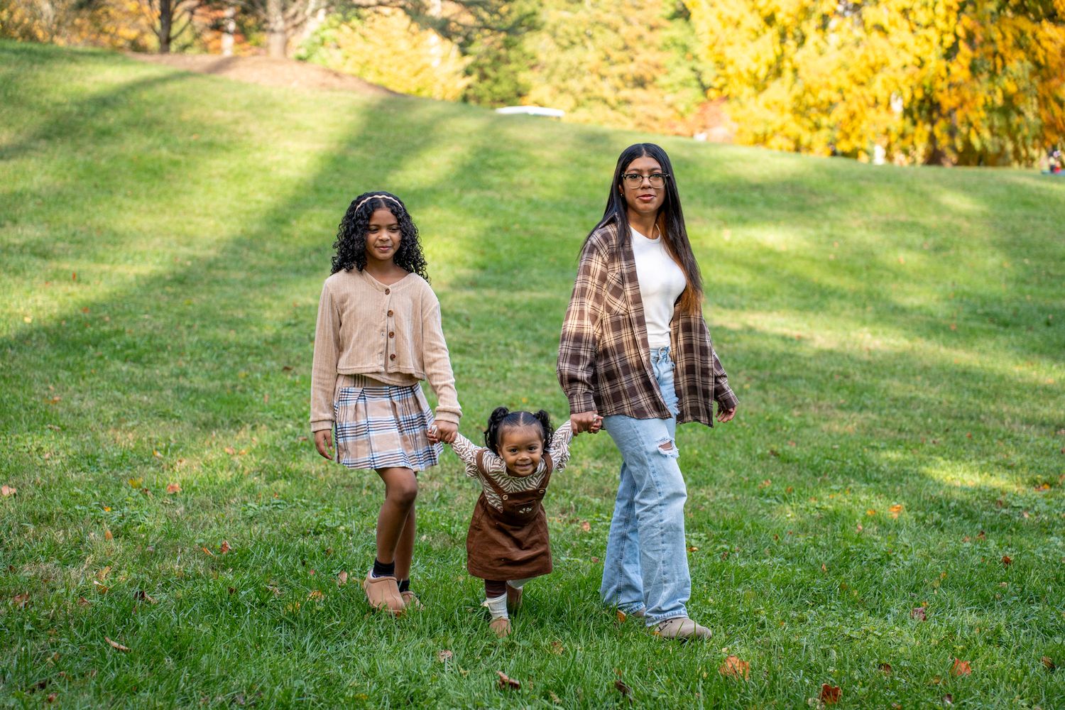Three people stand together on a grassy hill during autumn with golden trees in the background.