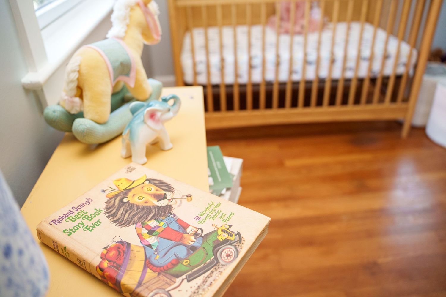 Vintage children's books and toys displayed on a wooden floor with a crib in the background.