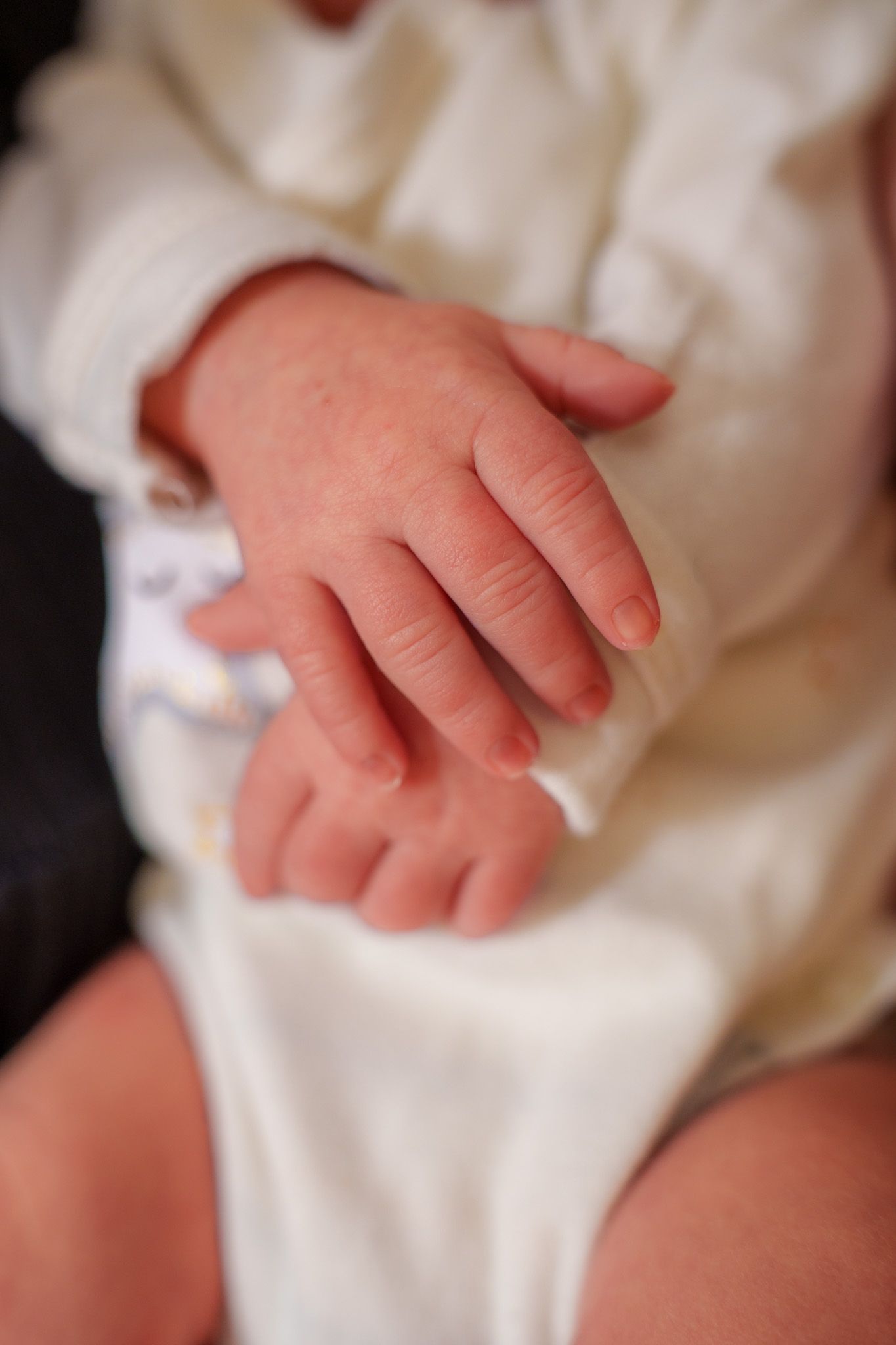 Close-up of a tiny baby's hand resting on soft white fabric, showing delicate pink skin and tiny fingers.