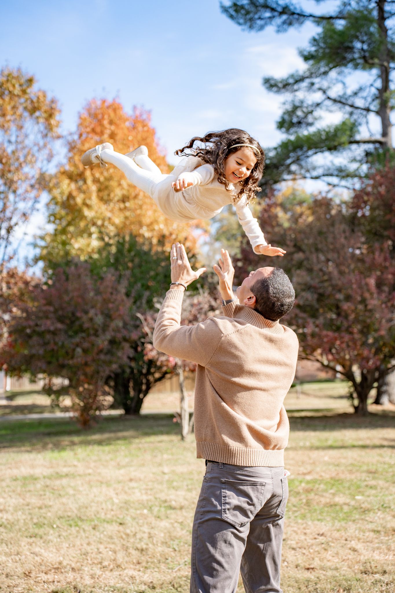 A parent and child share a joyful moment playing together in a park during autumn with fall foliage in the background.