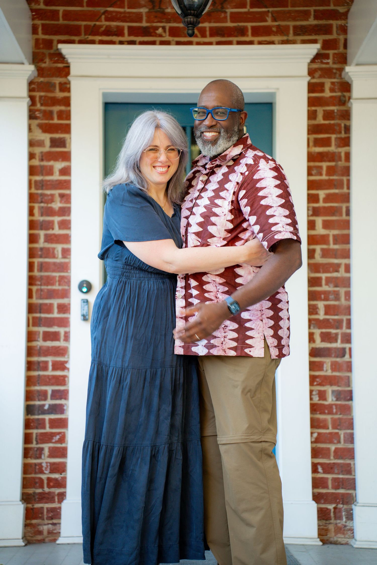 A couple embraces on a front porch with white columns and red brick walls in a series of candid photos.