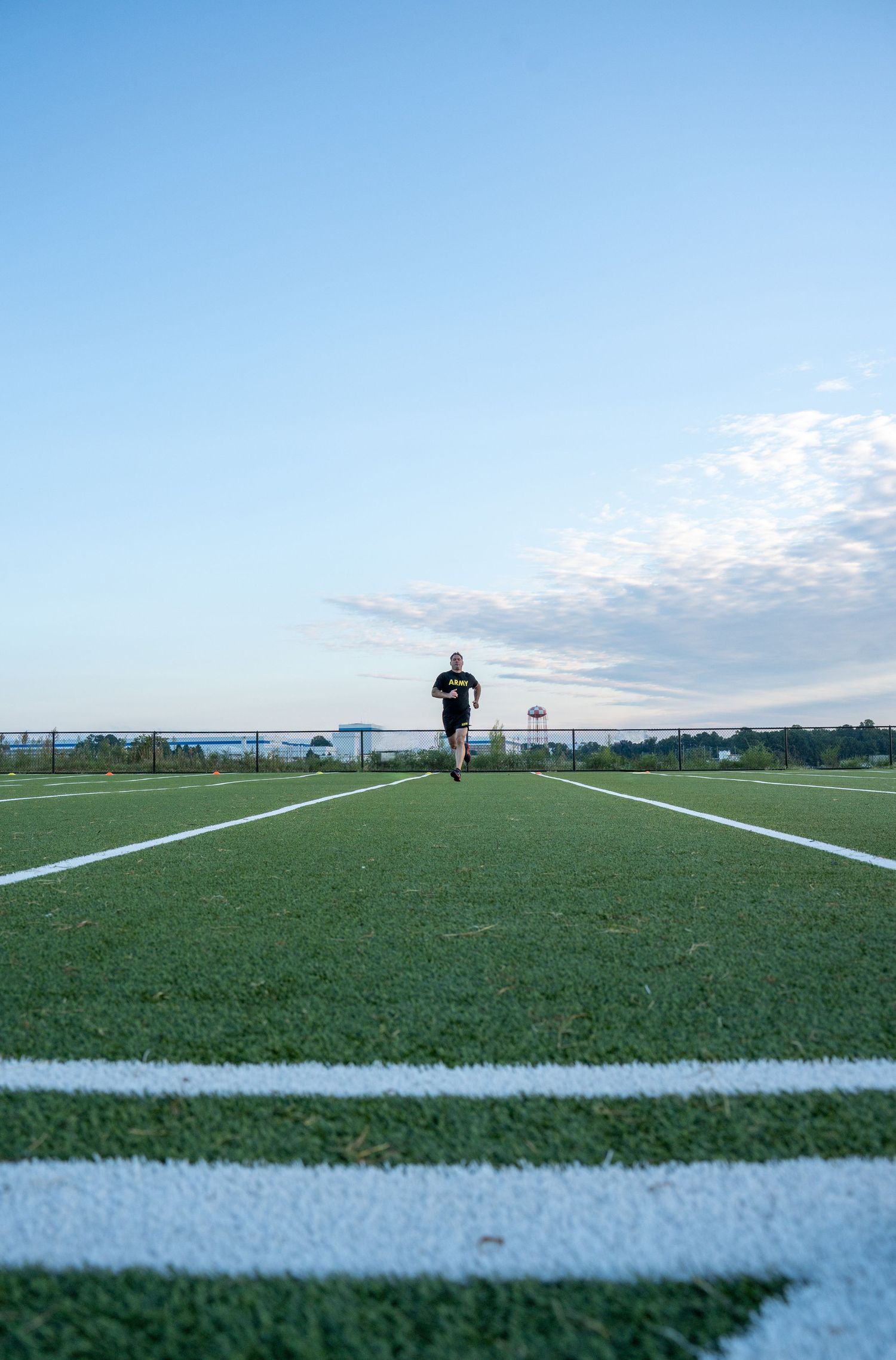 Soccer field lines painted on artificial turf with goal posts visible in the distance under a blue sky.