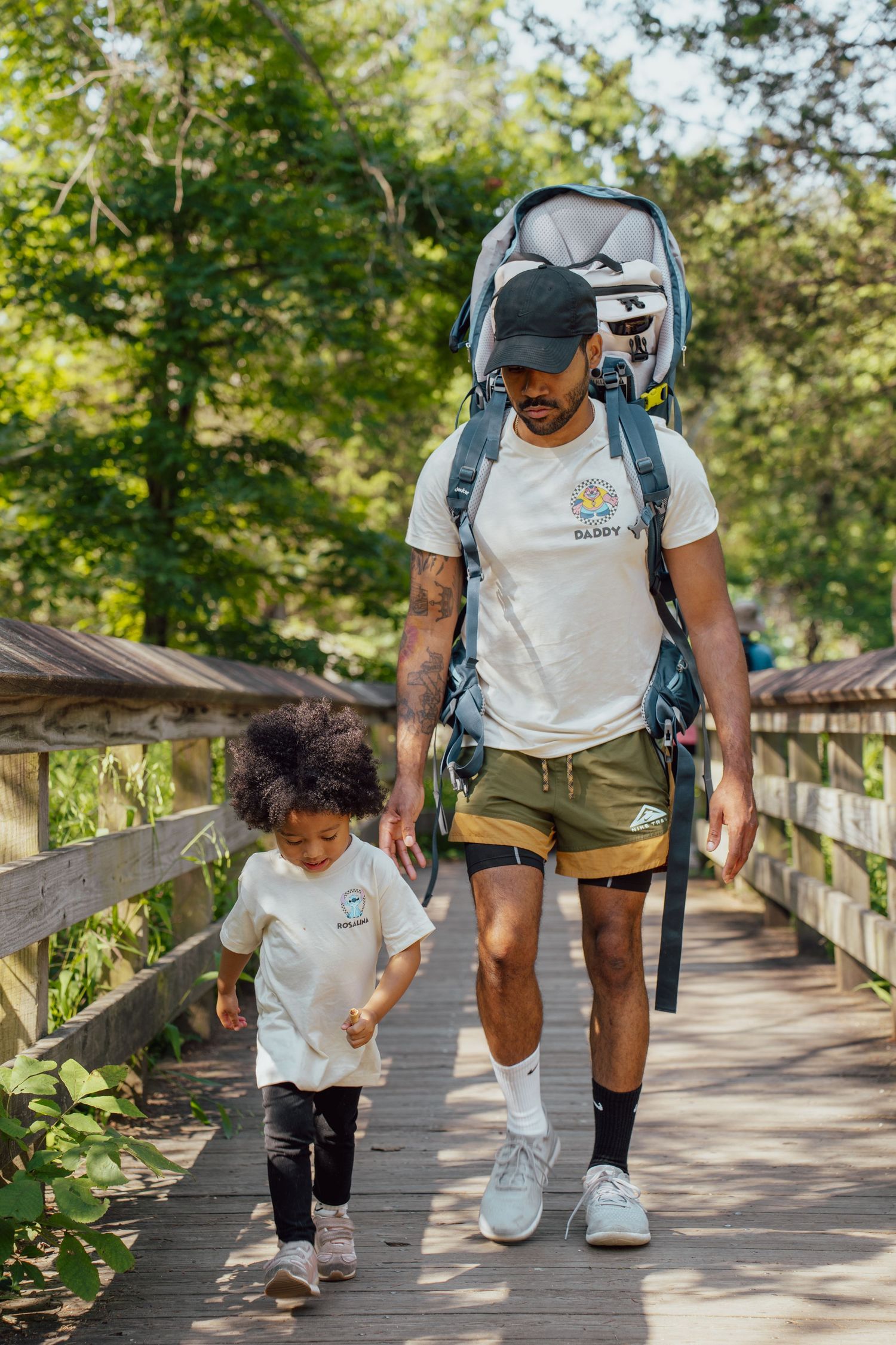 Adult and child walking together on wooden boardwalk path through nature.
