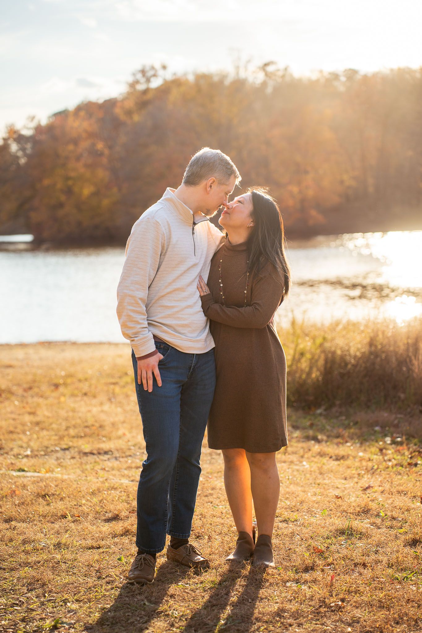 A couple embraces in a golden field at sunset during an autumn engagement photoshoot.