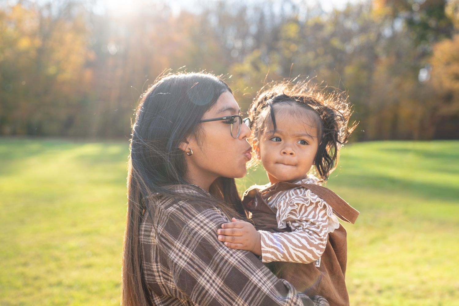 Parent and child share tender moments in a sunlit autumn field during golden hour photo session.