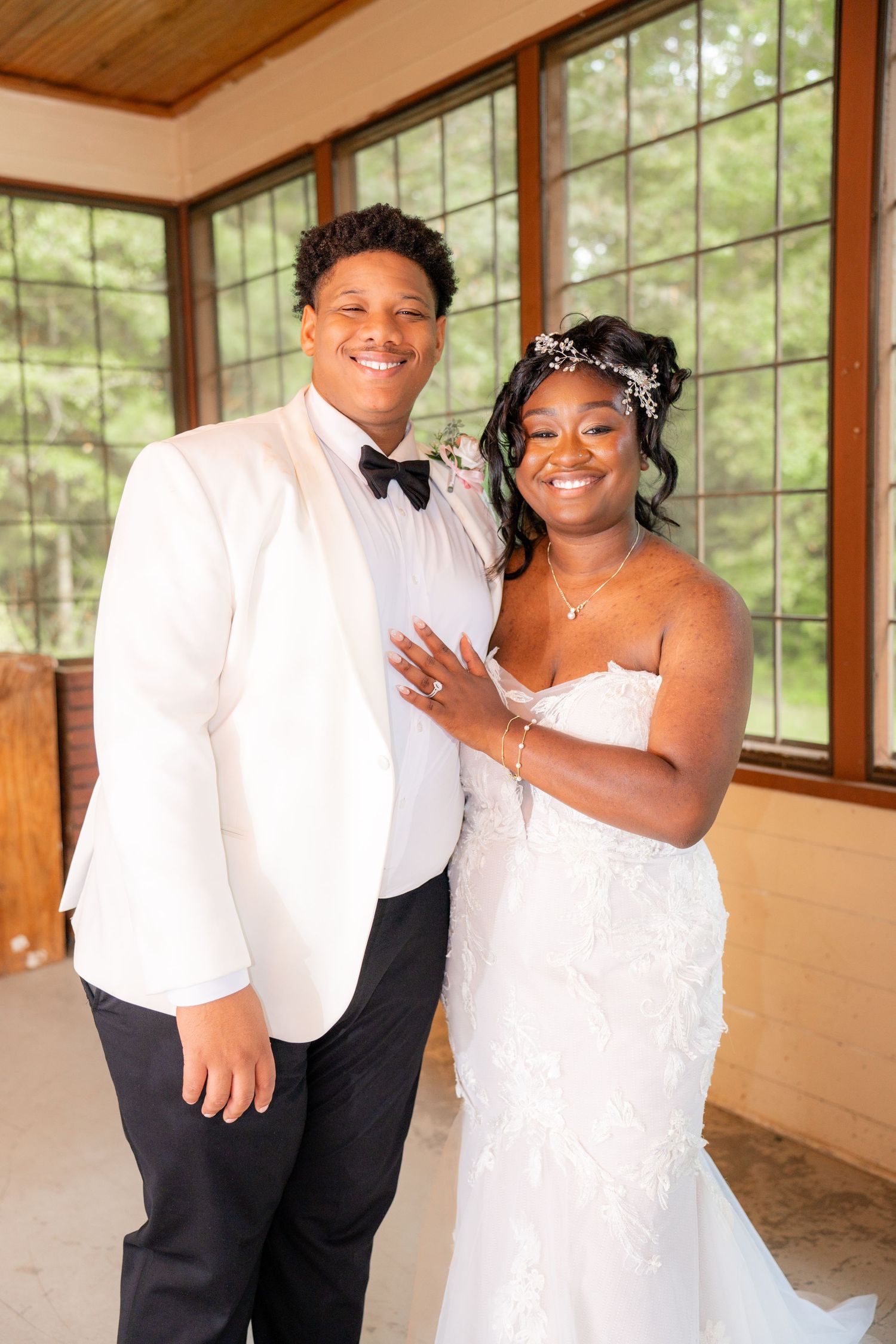 Wedding couple posing inside a rustic venue with large windows and wooden beams.