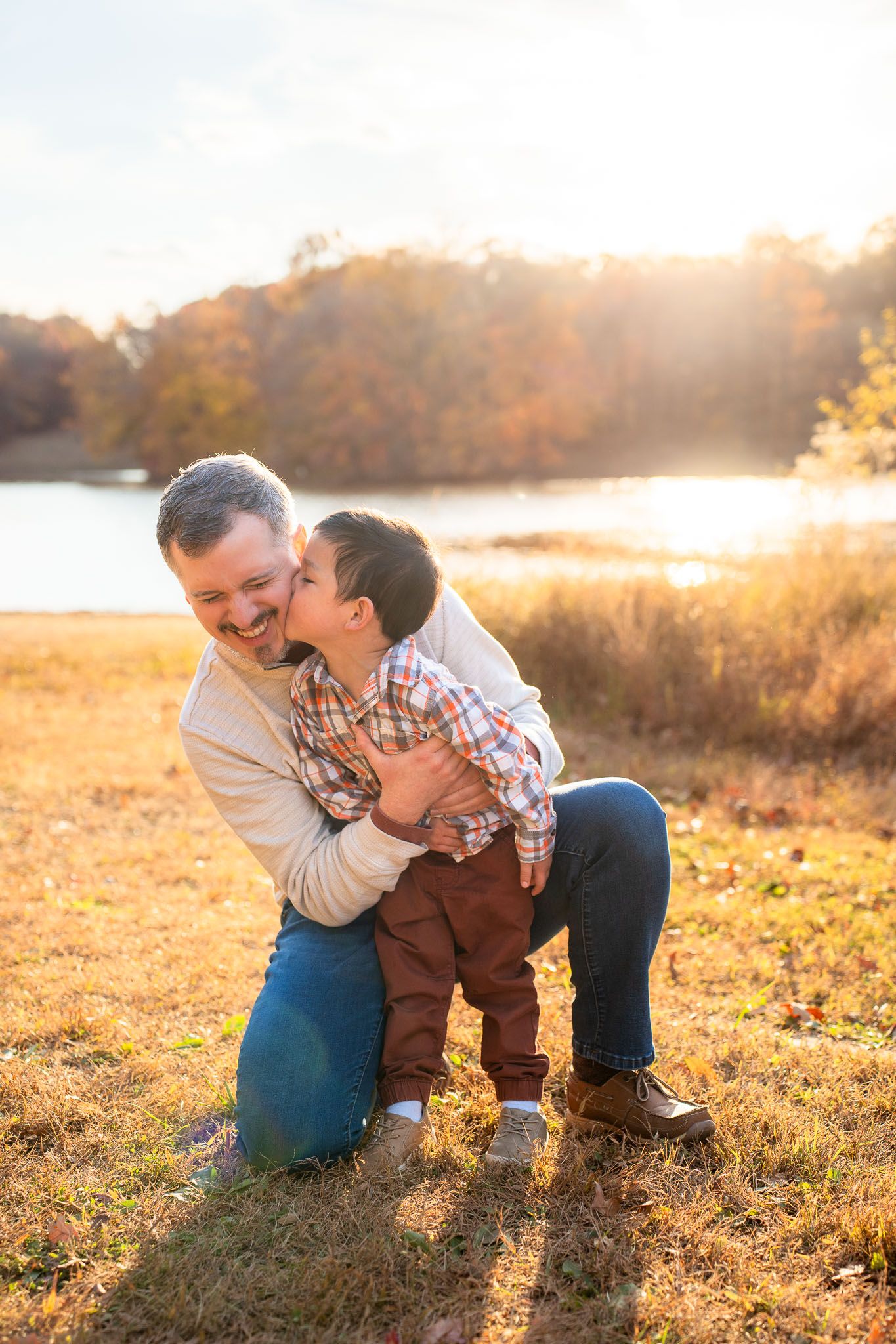 A tender moment of laughter and embrace captured in golden sunset light by the water.